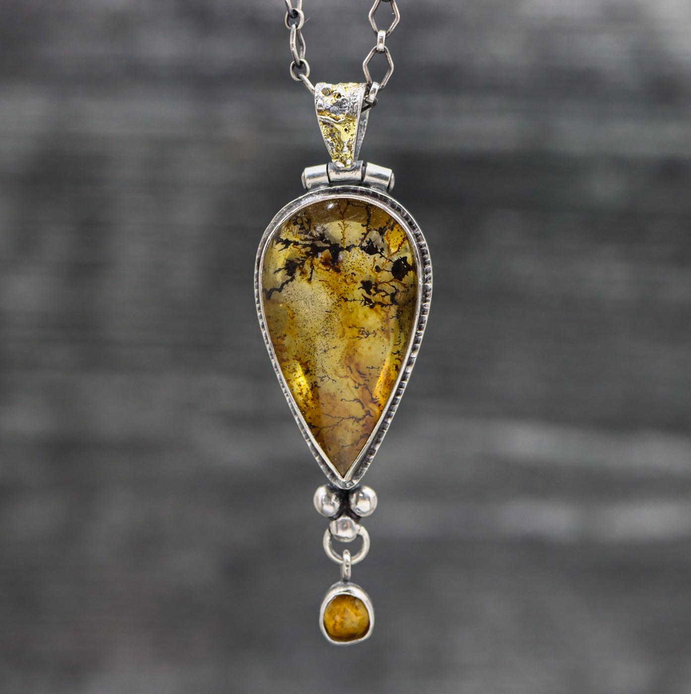 A sterling silver pendant featuring a dendritic quartz with iron staining and a faceted rose cut mandarine citrine below, with a textured bail and gold accents.