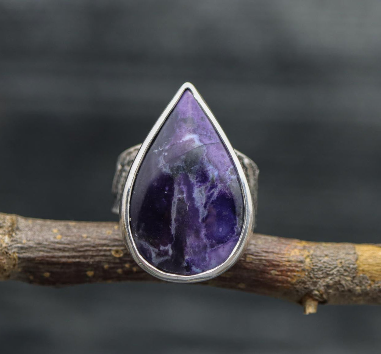 A sterling silver wide band ring with a teardrop-shaped purple Tiffany stone, set in a double bezel, on a branch.