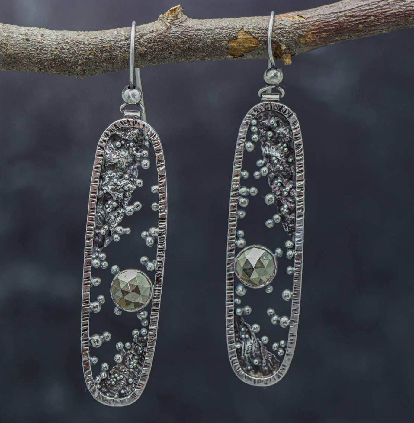 A pair of silver earrings with reticulated and granulated designs, displayed against a dark background.