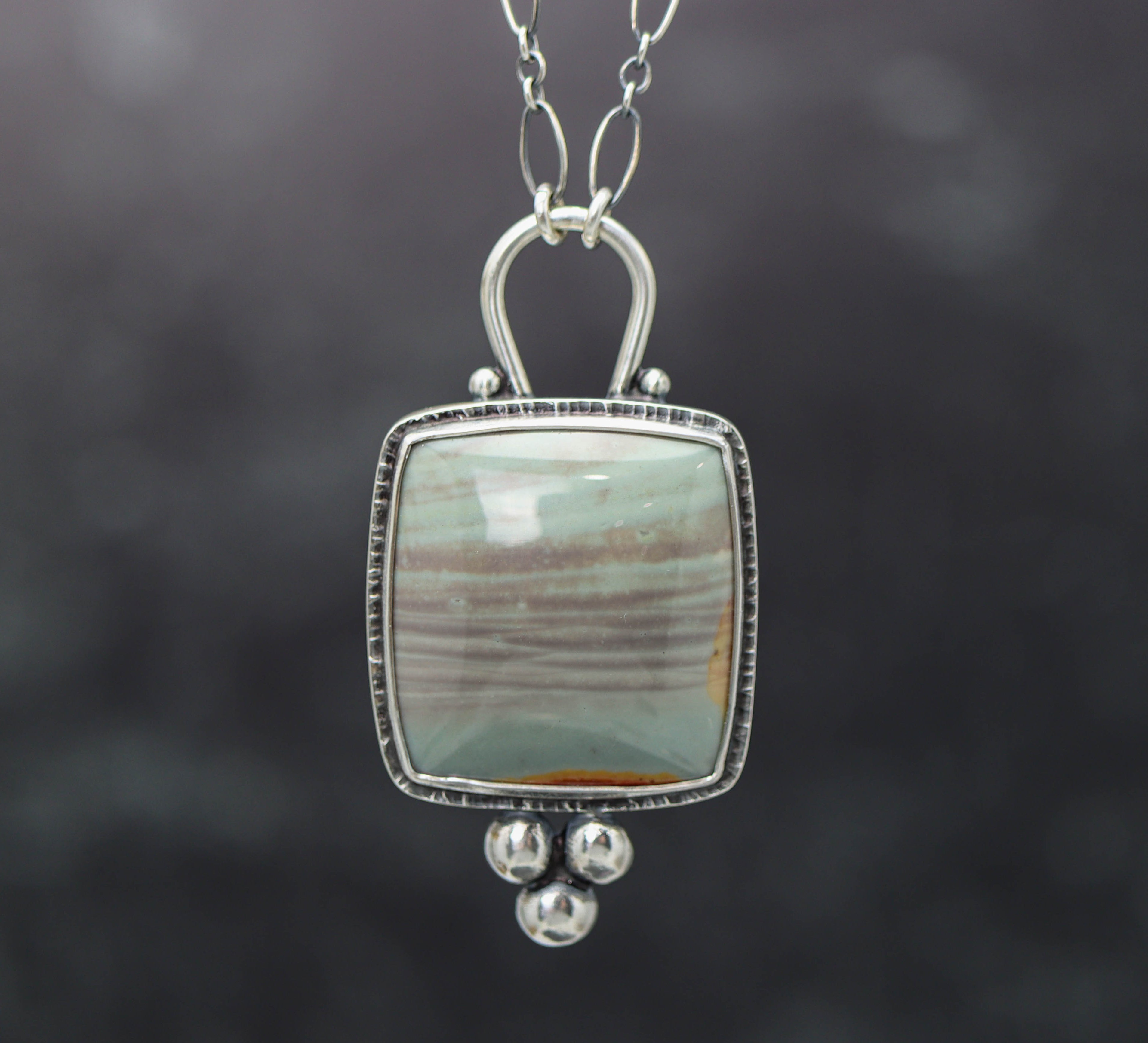 A polychrome jasper gemstone pendant set in a sterling silver double bezel setting with a lobster claw closure on an oval-shaped chain.