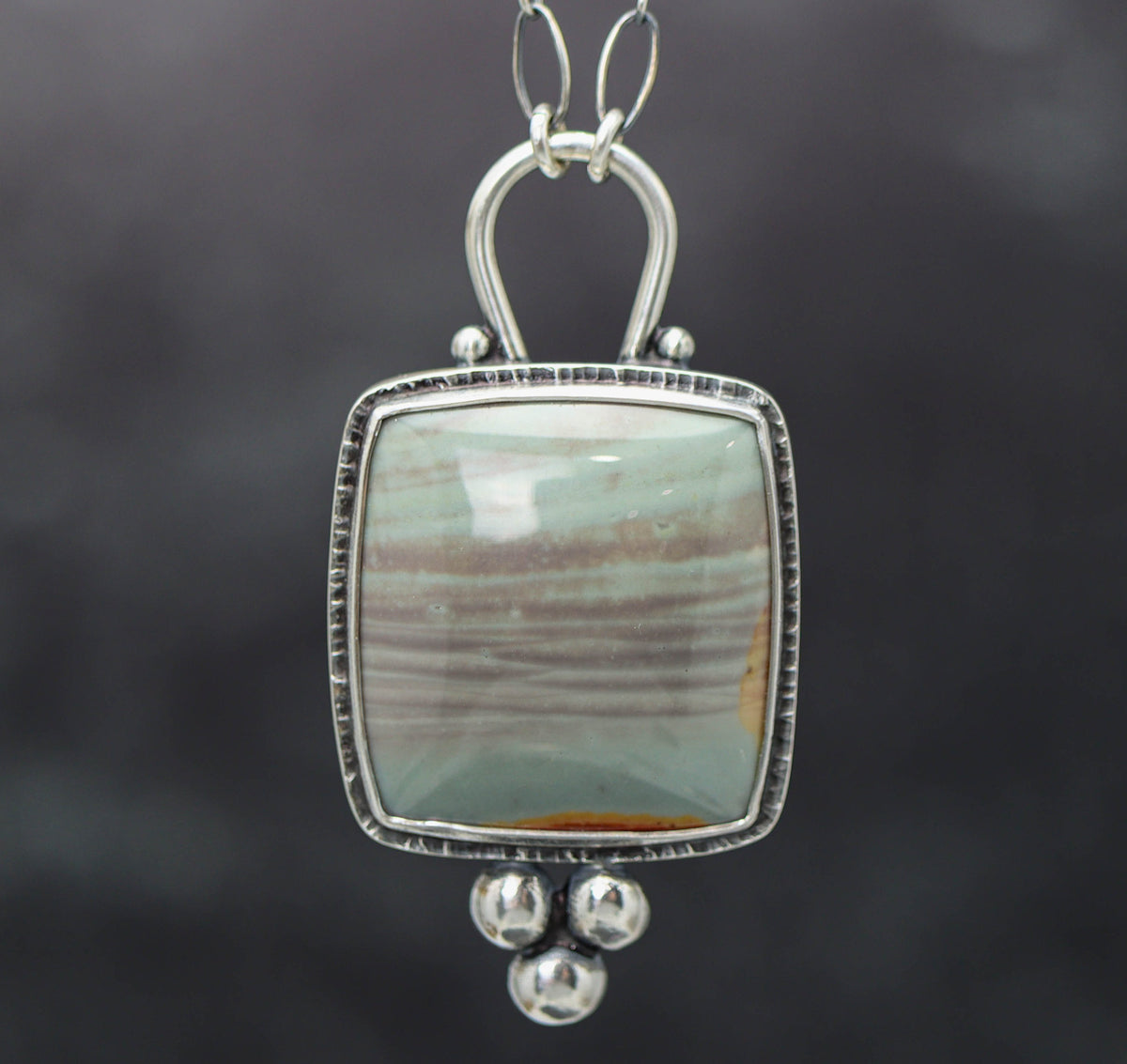 A polychrome jasper gemstone pendant set in a sterling silver double bezel setting with a lobster claw closure on an oval-shaped chain.