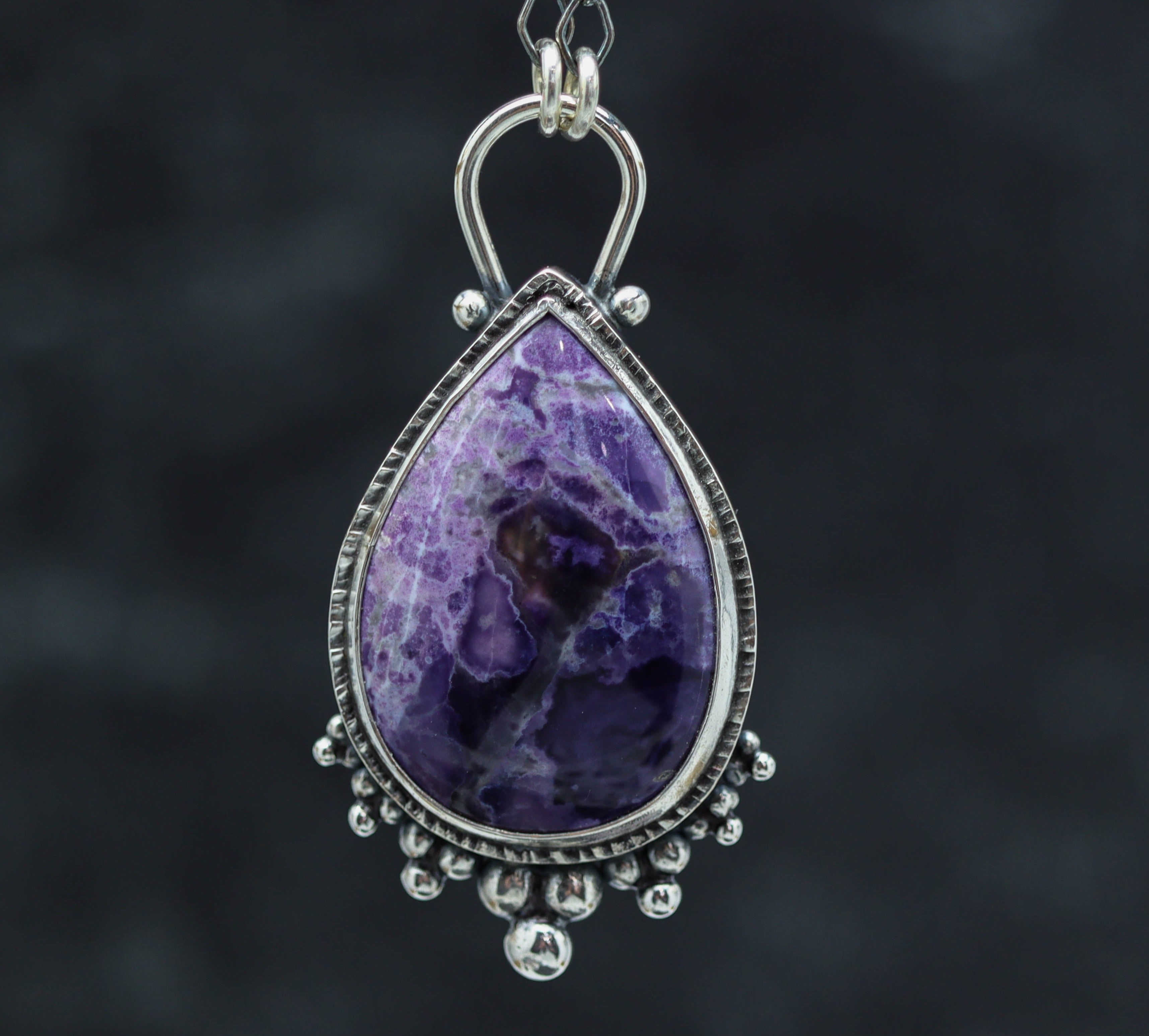 A sterling silver pendant featuring a large purple tiffany stone, with a textured metal design and small silver accents.