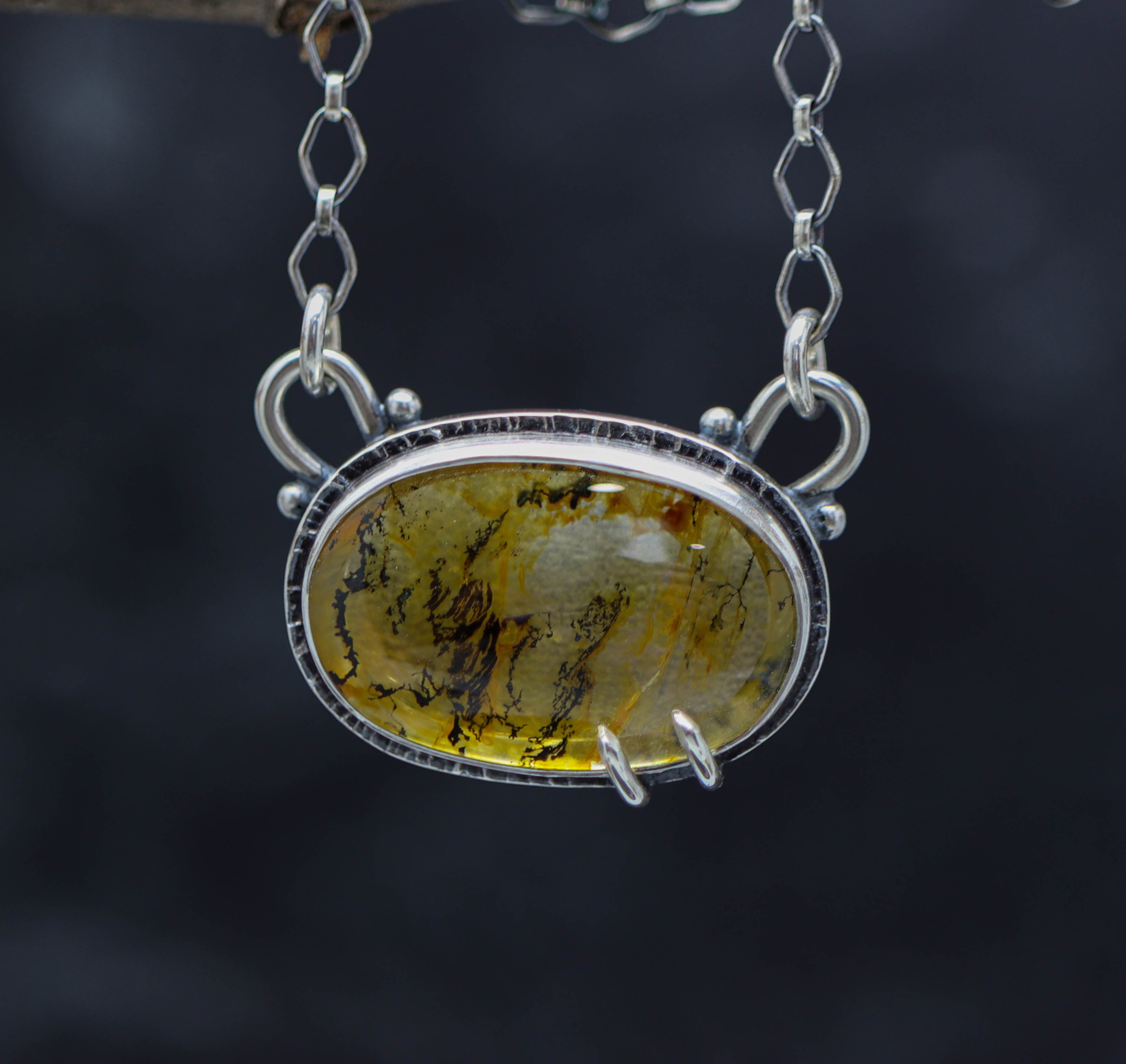 A dendritic quartz pendant set in a sterling silver double bezel pendant with a lobster claw closure on a chain.