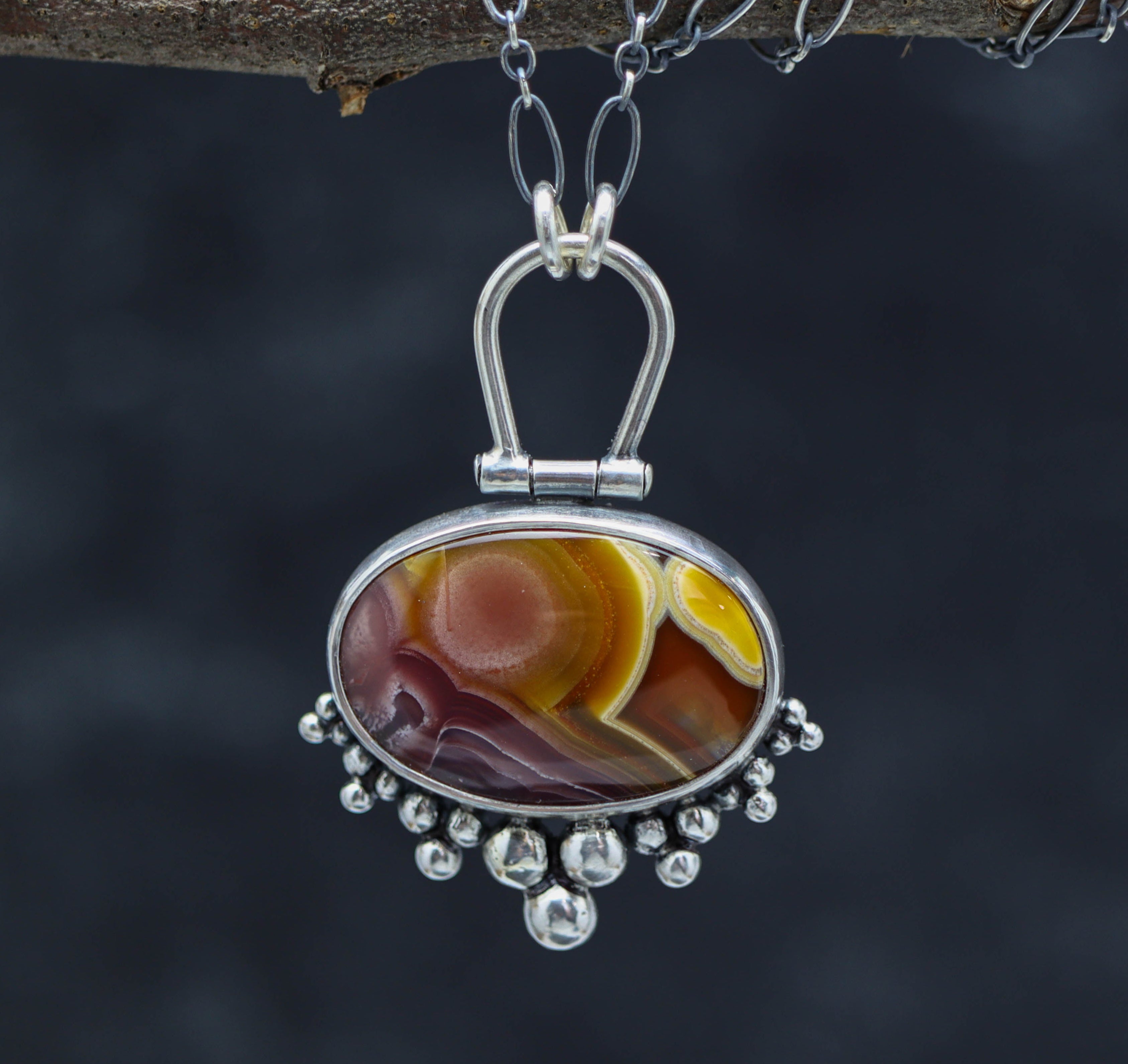 A sterling silver pendant featuring an Agua Nueva agate gemstone, with silver ball details and a ruffled silver bail, suspended by a silver chain.