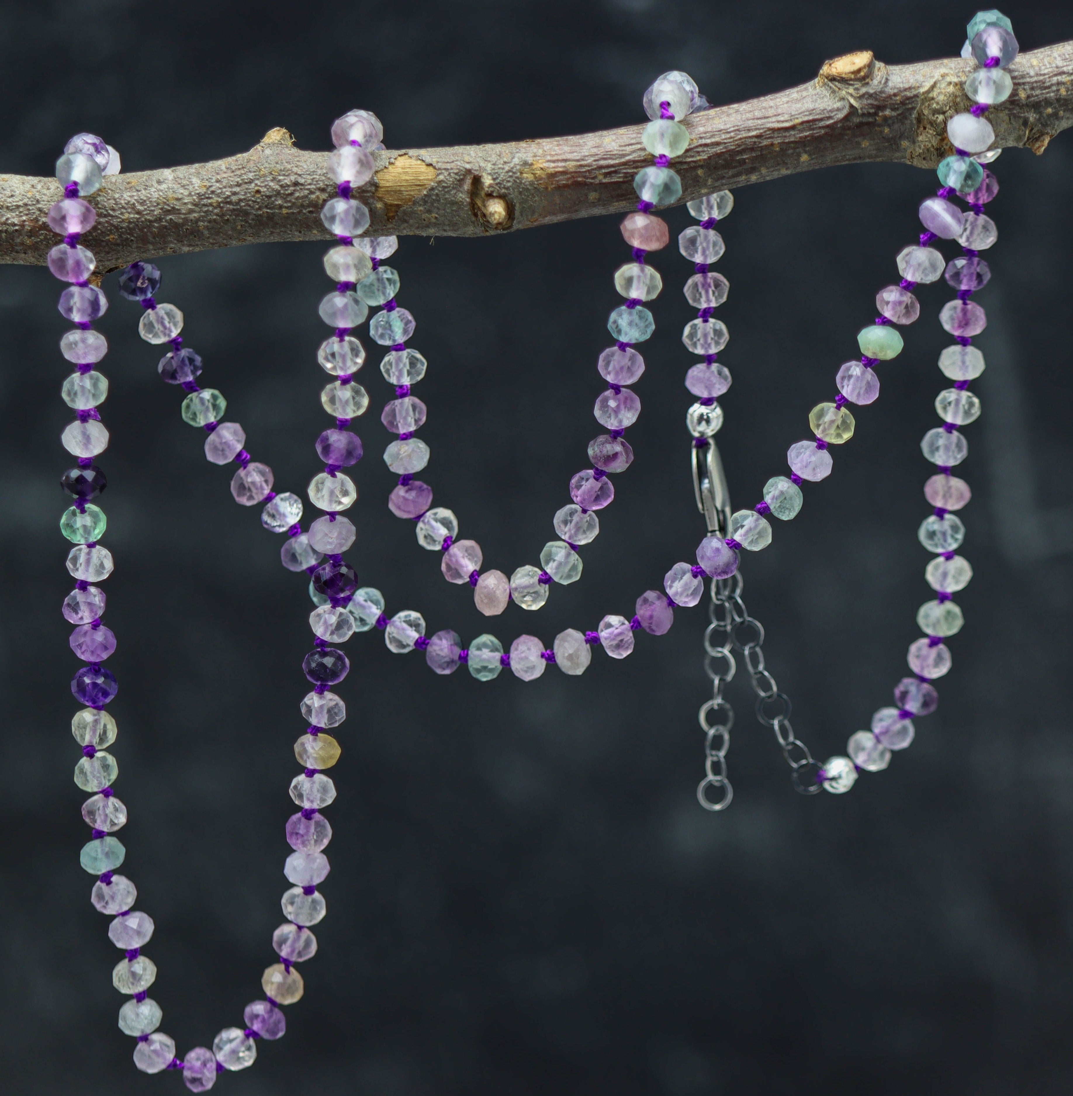 A sterling silver necklace featuring hand knotted silk thread and roundel-shaped rainbow fluorite beads with a lobster claw closure.
