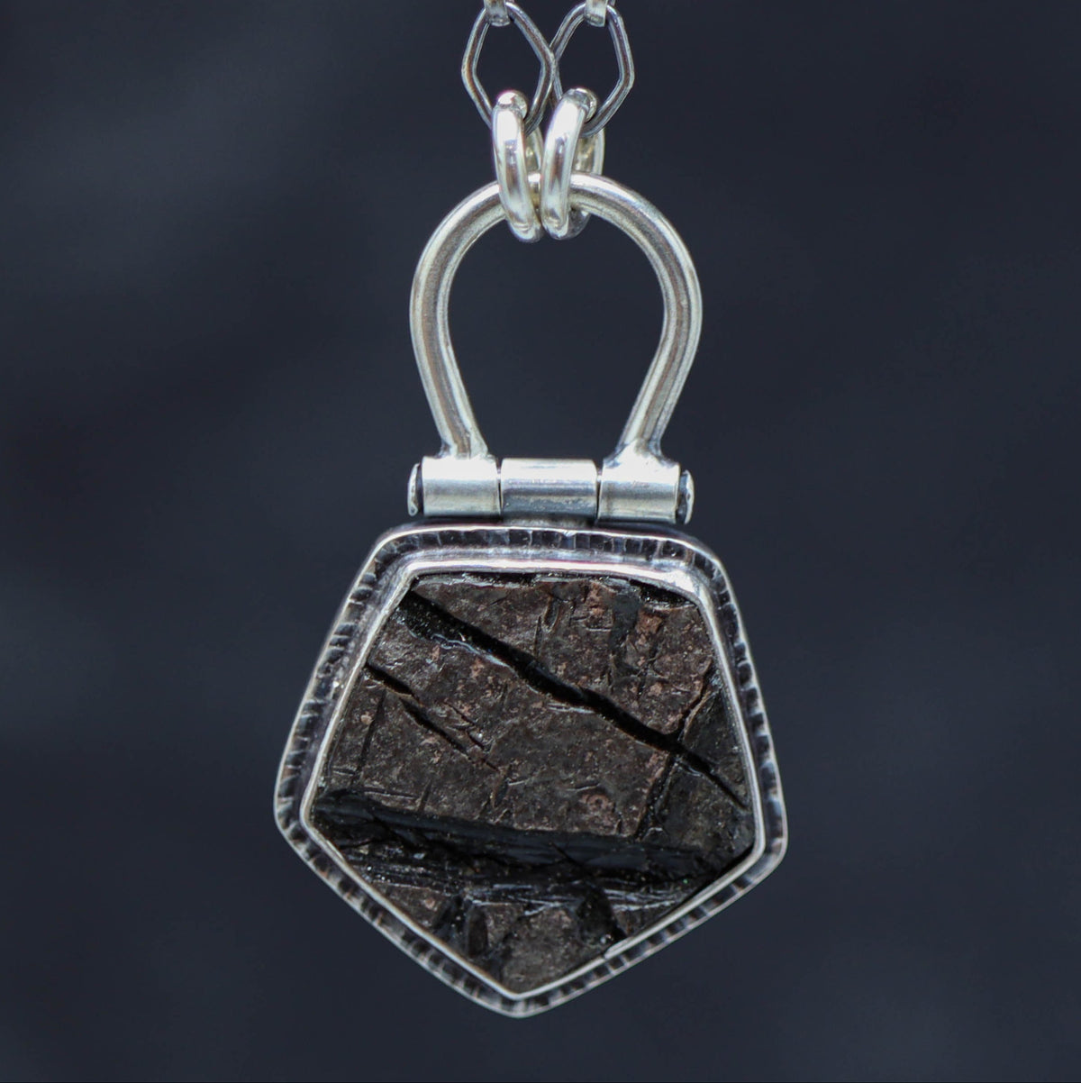 A sterling silver necklace with a natural surface obsidian pendant, displayed on a tree branch.