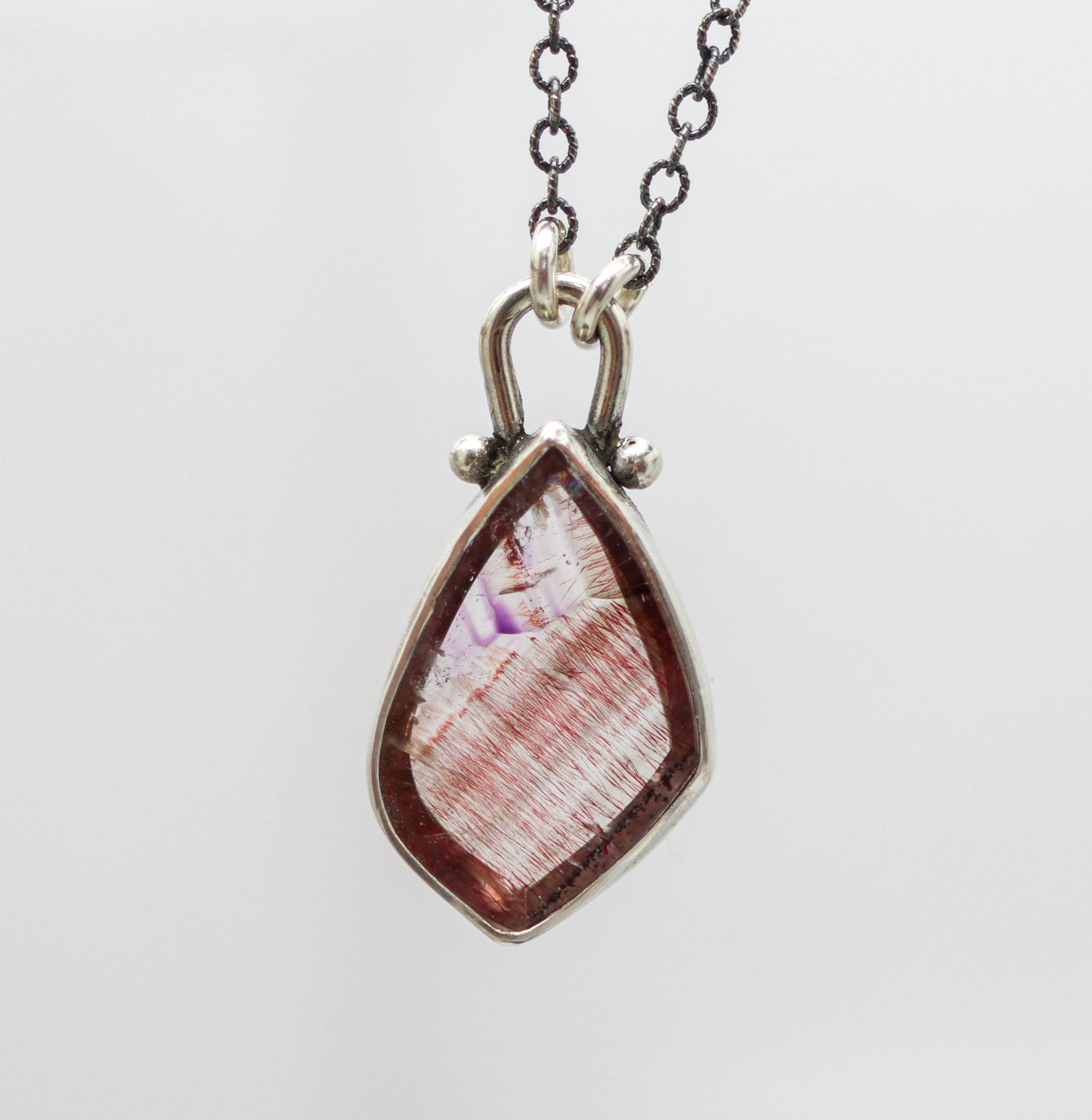 A sterling silver pendant featuring a multicolored gemstone, suspended from a silver chain.