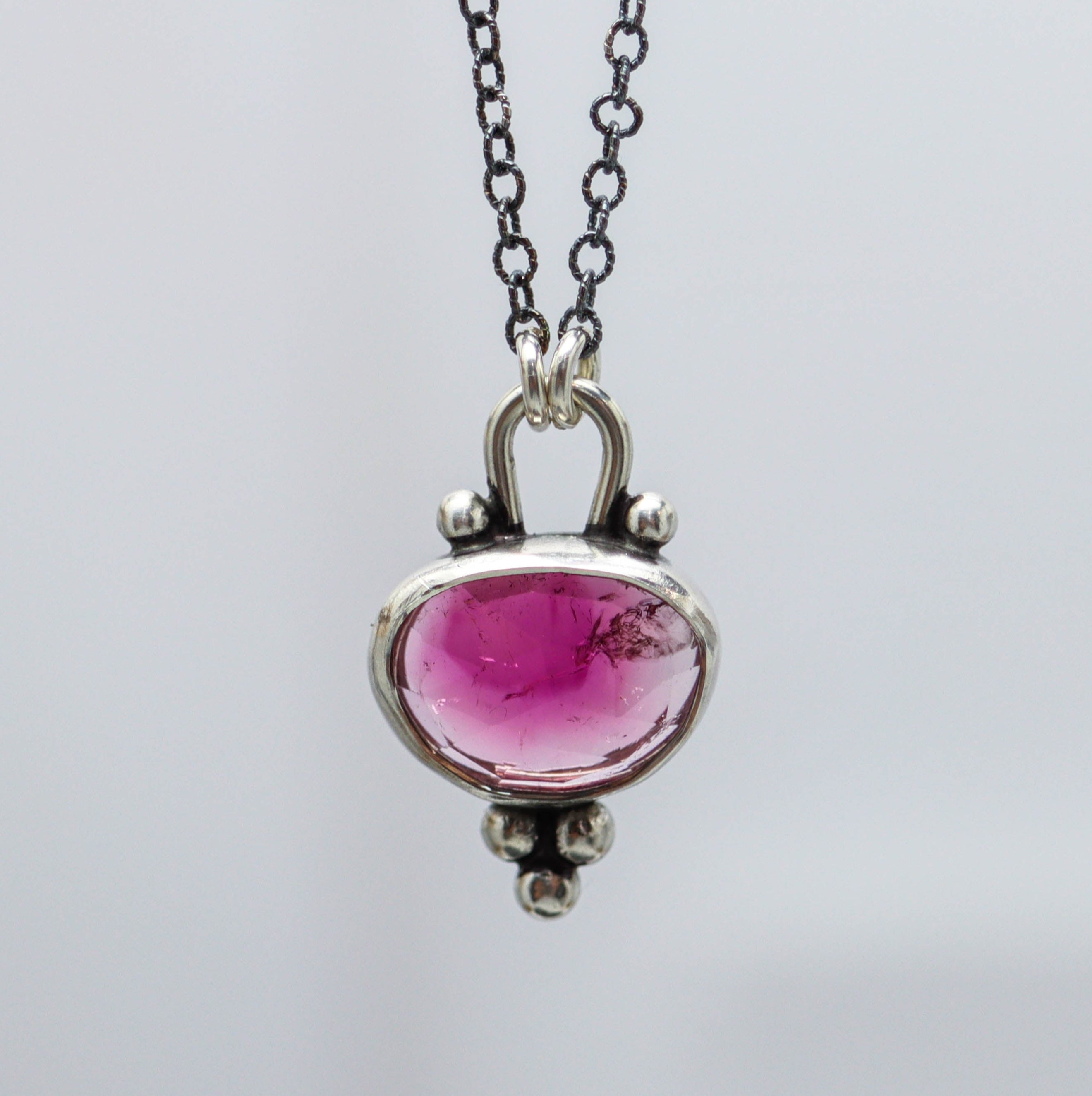 A sterling silver pendant necklace featuring a rose-cut pink tourmaline centerpiece, with ball details and a lobster claw closure.