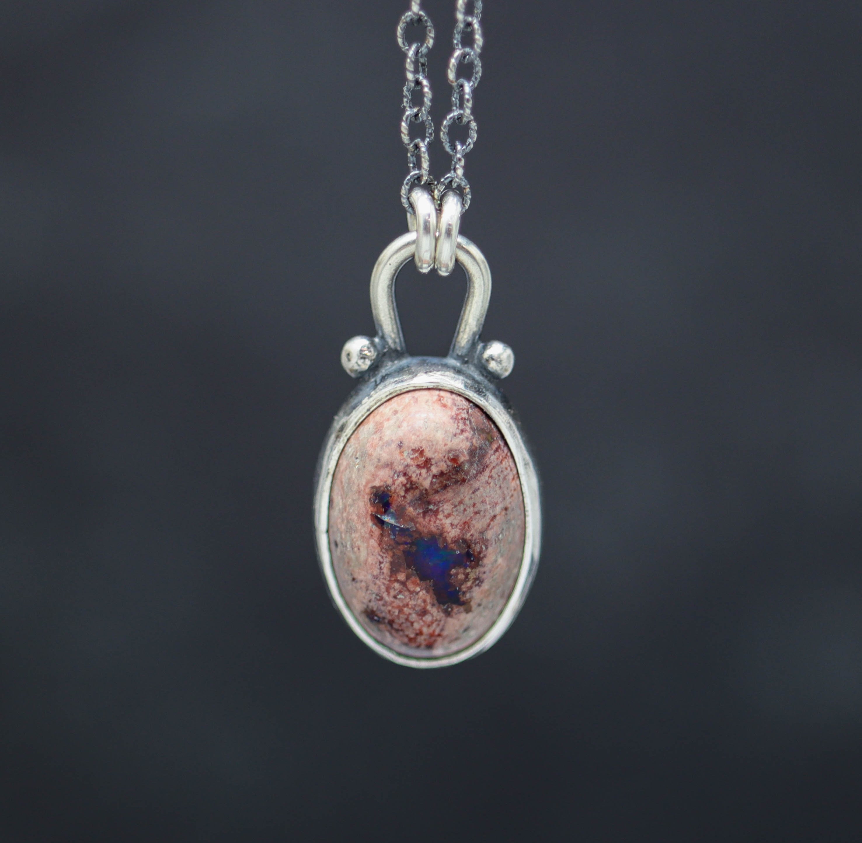 A sterling silver pendant necklace with a Mexican fire opal set in a silver setting, displayed against a dark background.