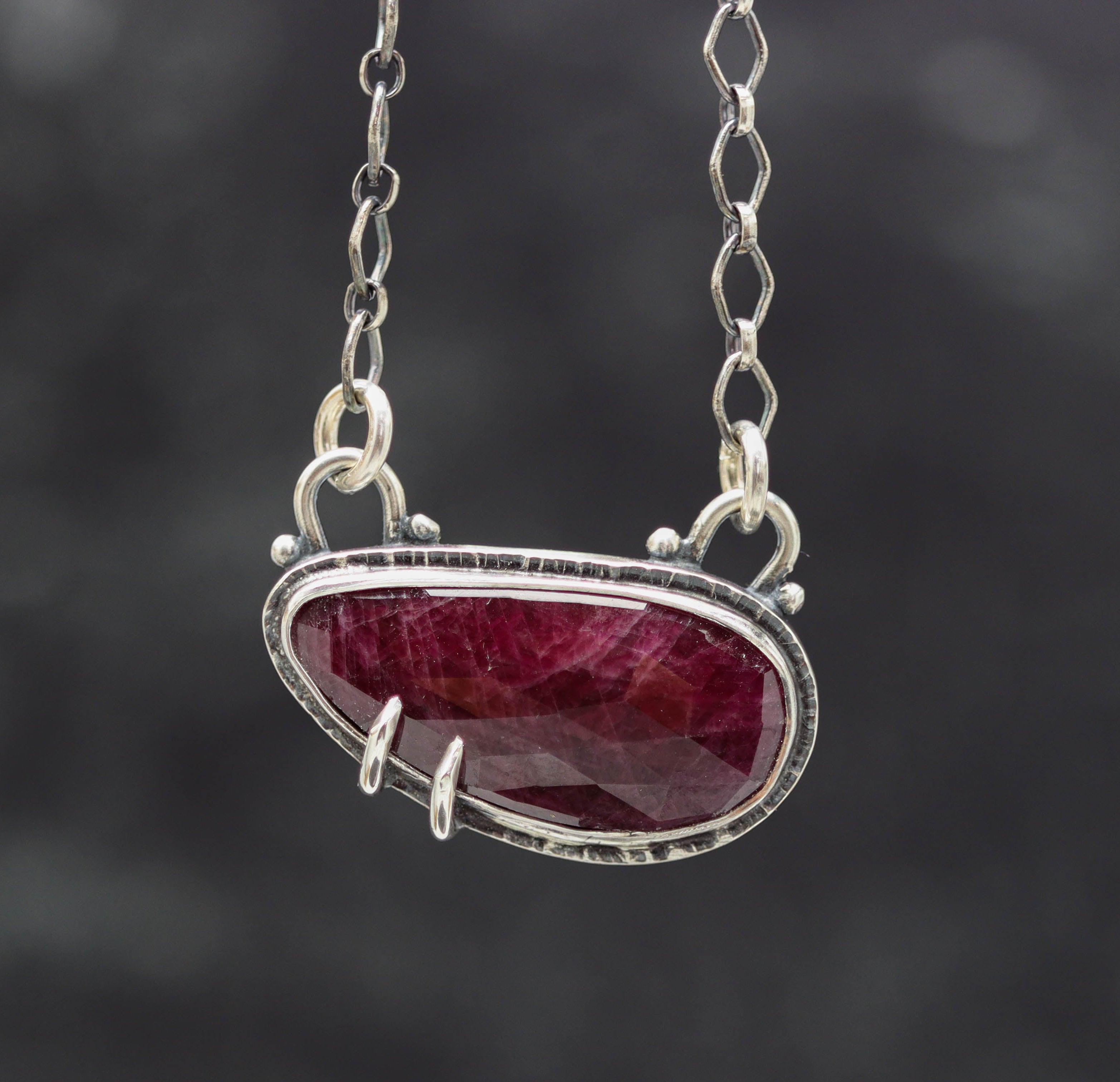 A red ruby pendant sterling silver necklace with a double bezel and prongs, suspended by a sterling silver chain.
