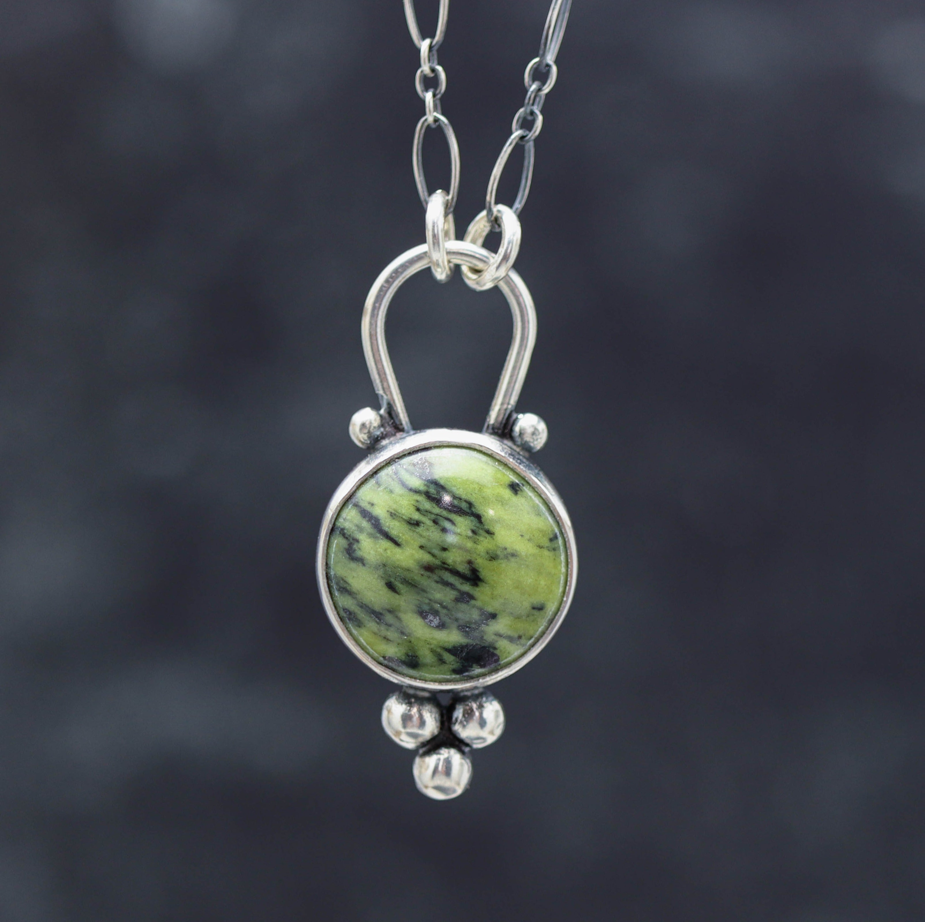 A green serpentine pendant with a sterling silver metal setting, attached to a silver chain.