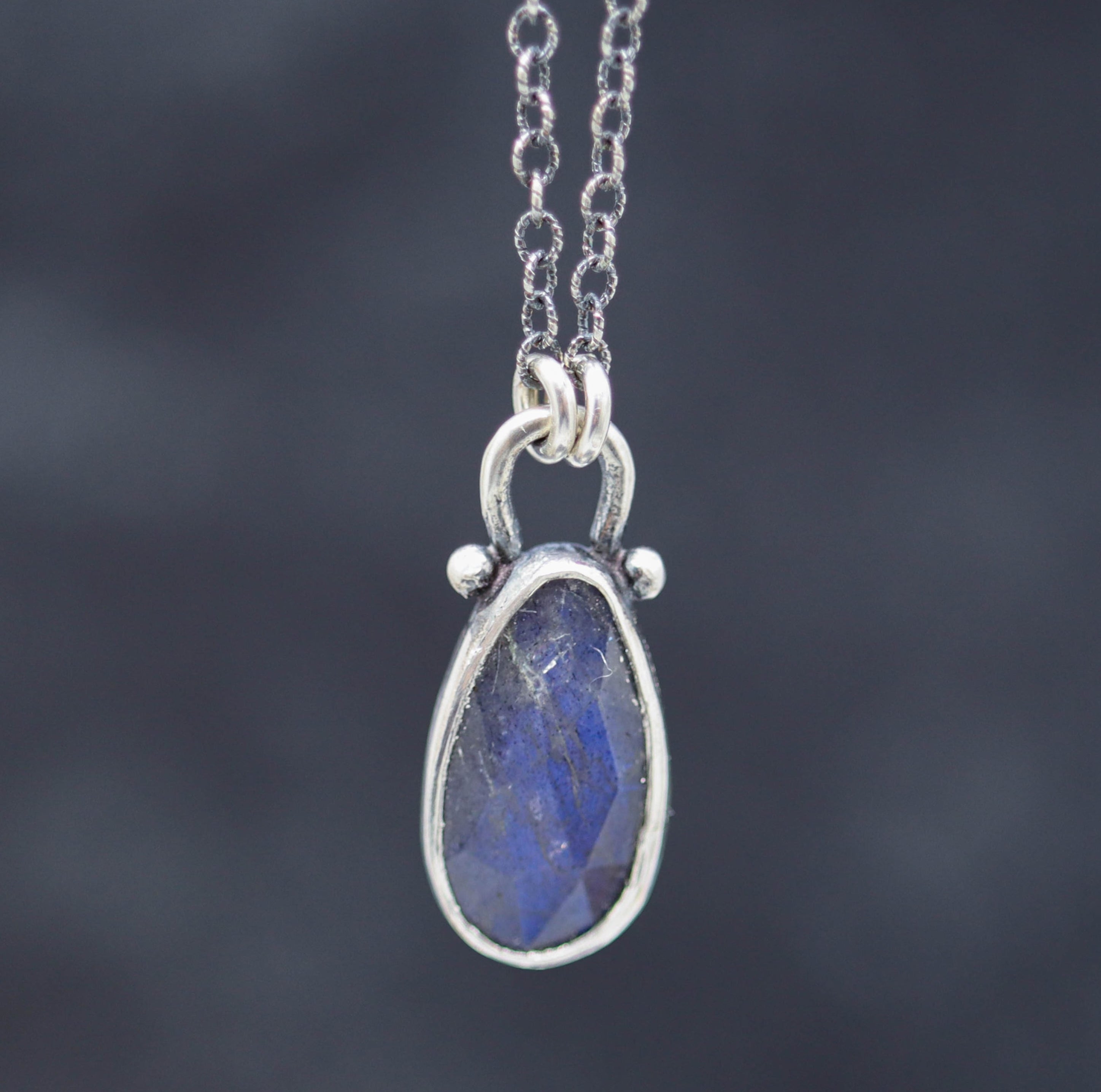 A sterling silver pendant necklace with a faceted rose cut labradorite gemstone, displayed against a blurred background.
