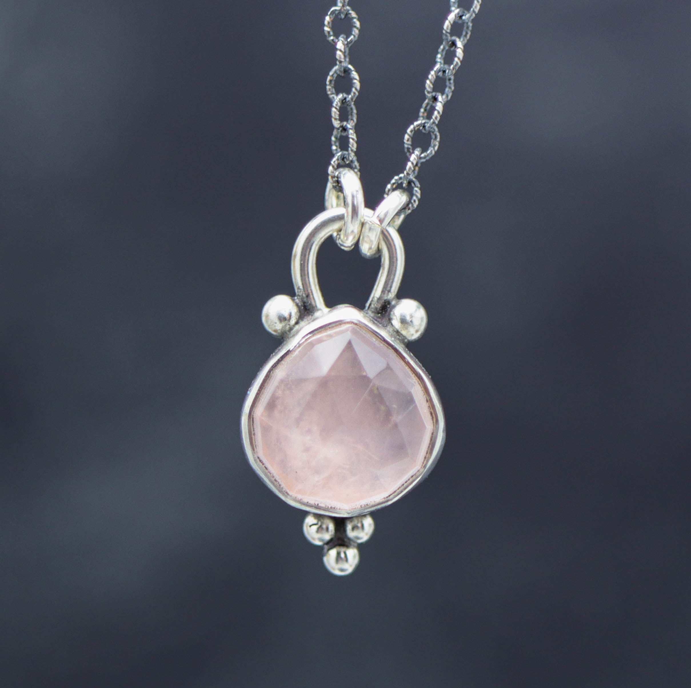 A sterling silver pendant necklace featuring a rose quartz gemstone with small silver ball accents, displayed against a misty background.