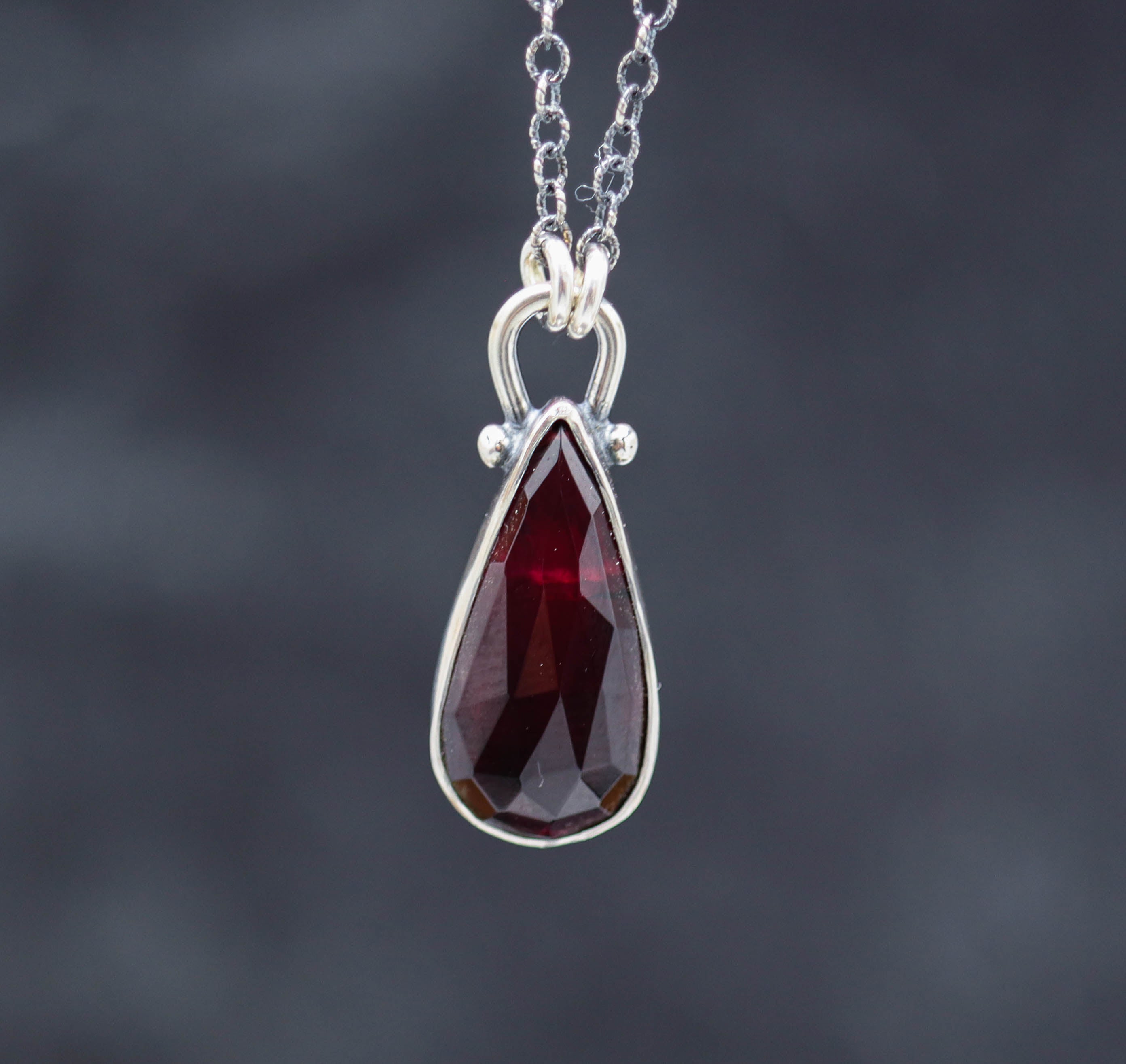 A red garnet pendant necklace with small silver ball accents, displayed on a sterling silver chain.