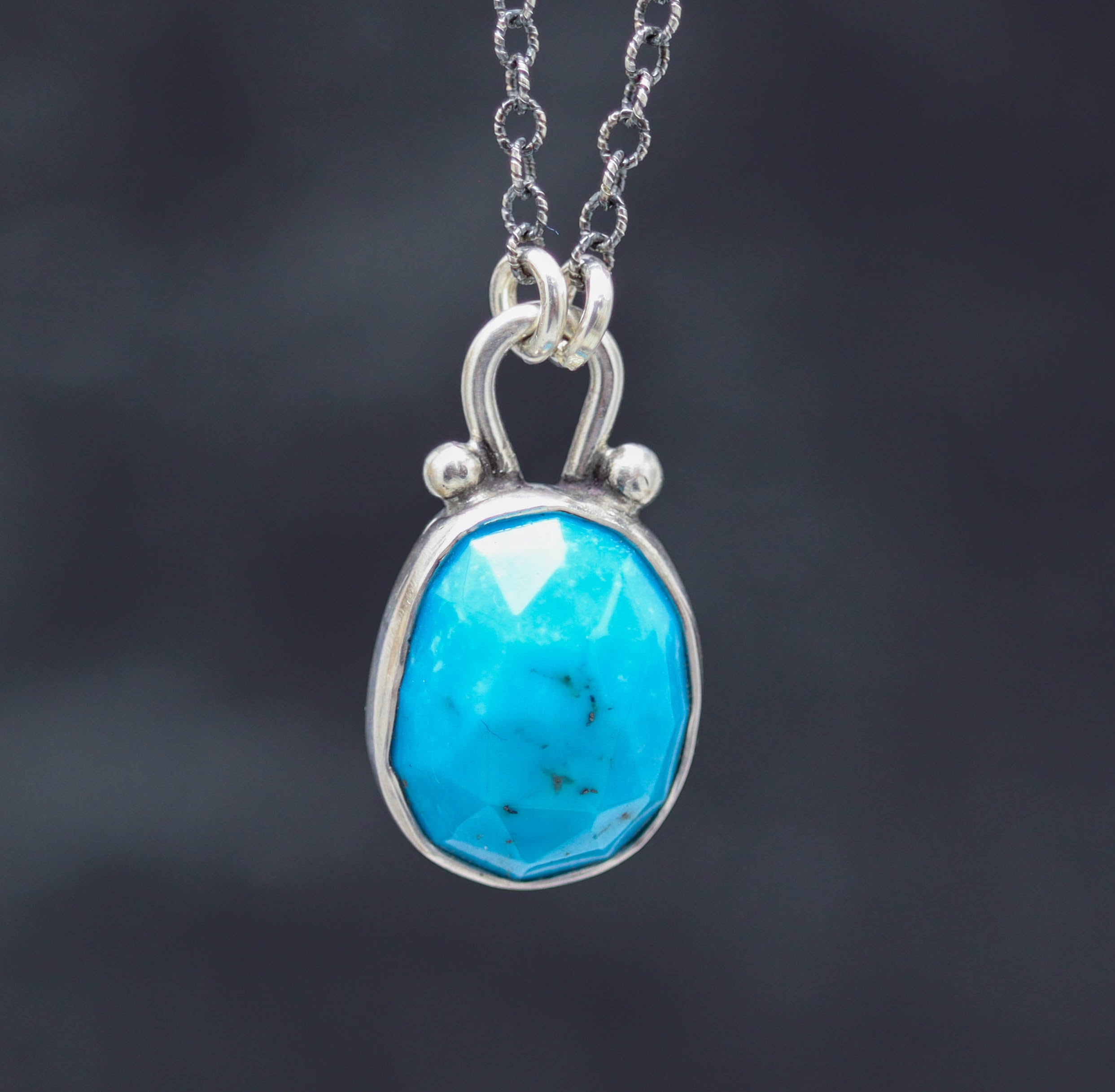 A sterling silver pendant necklace with a faceted bright blue turquoise centerpiece, surrounded by silver ball accents, on an oxidized cable link chain with a lobster claw closure.
