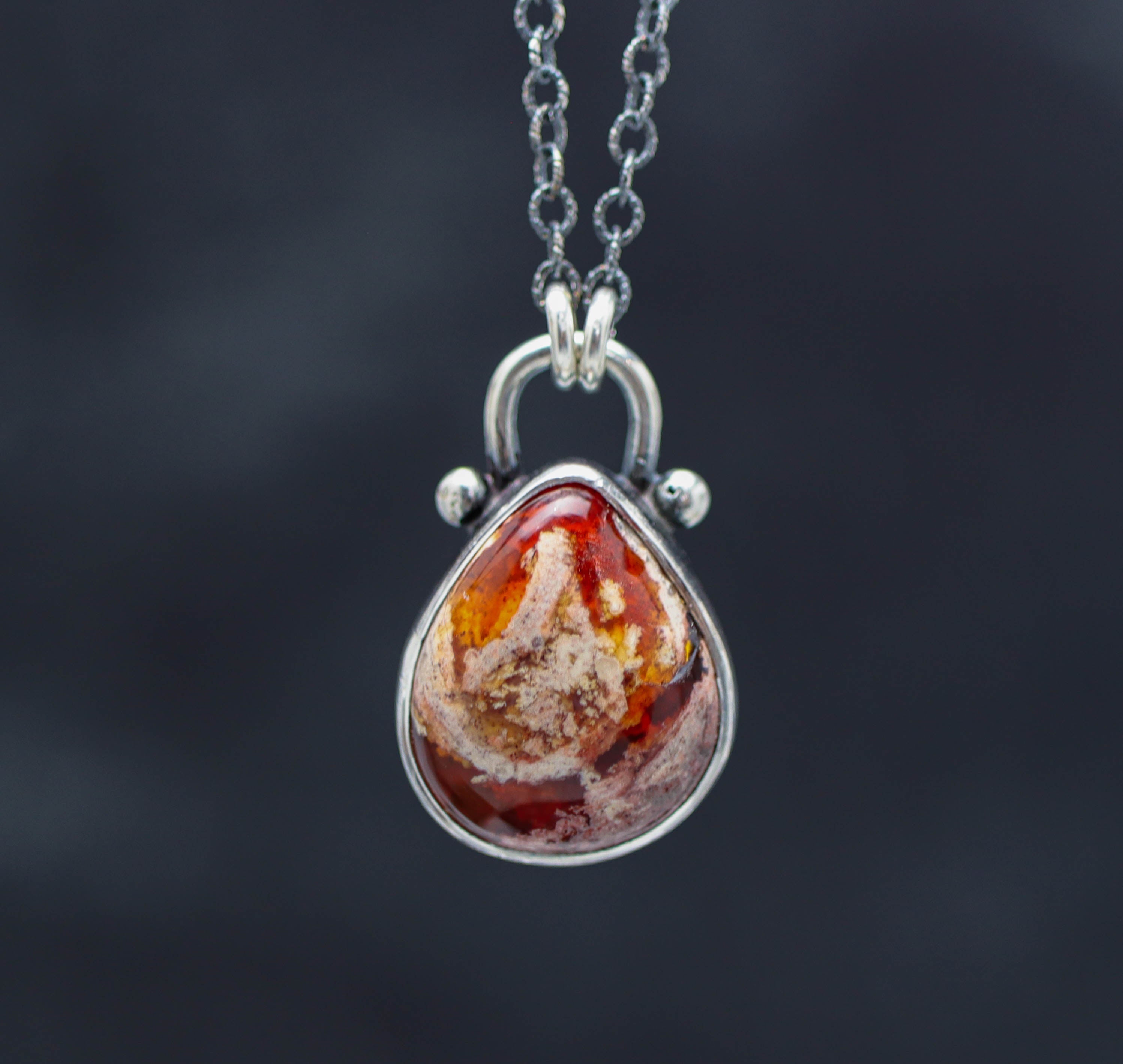 A sterling silver pendant necklace featuring a Mexican fire opal gemstone with a red and orange hue, suspended from a silver cable link chain.