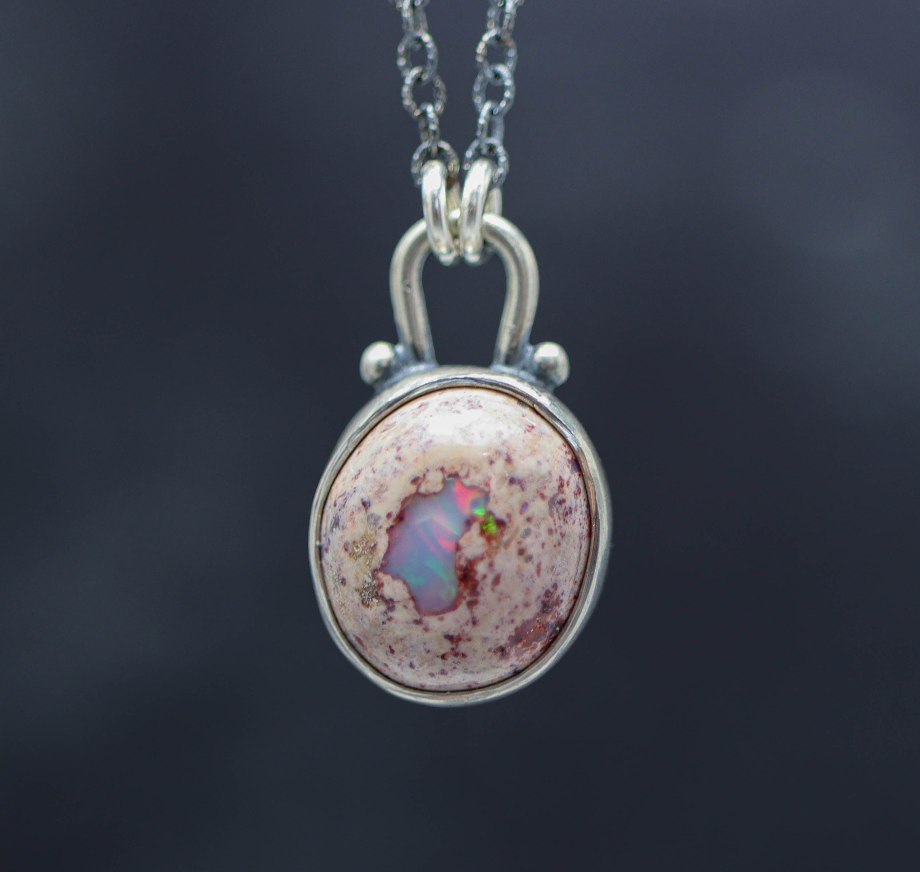 A sterling silver pendant necklace featuring a Mexican fire opal with a rainbow flashy white appearance, suspended from a silver cable link chain.