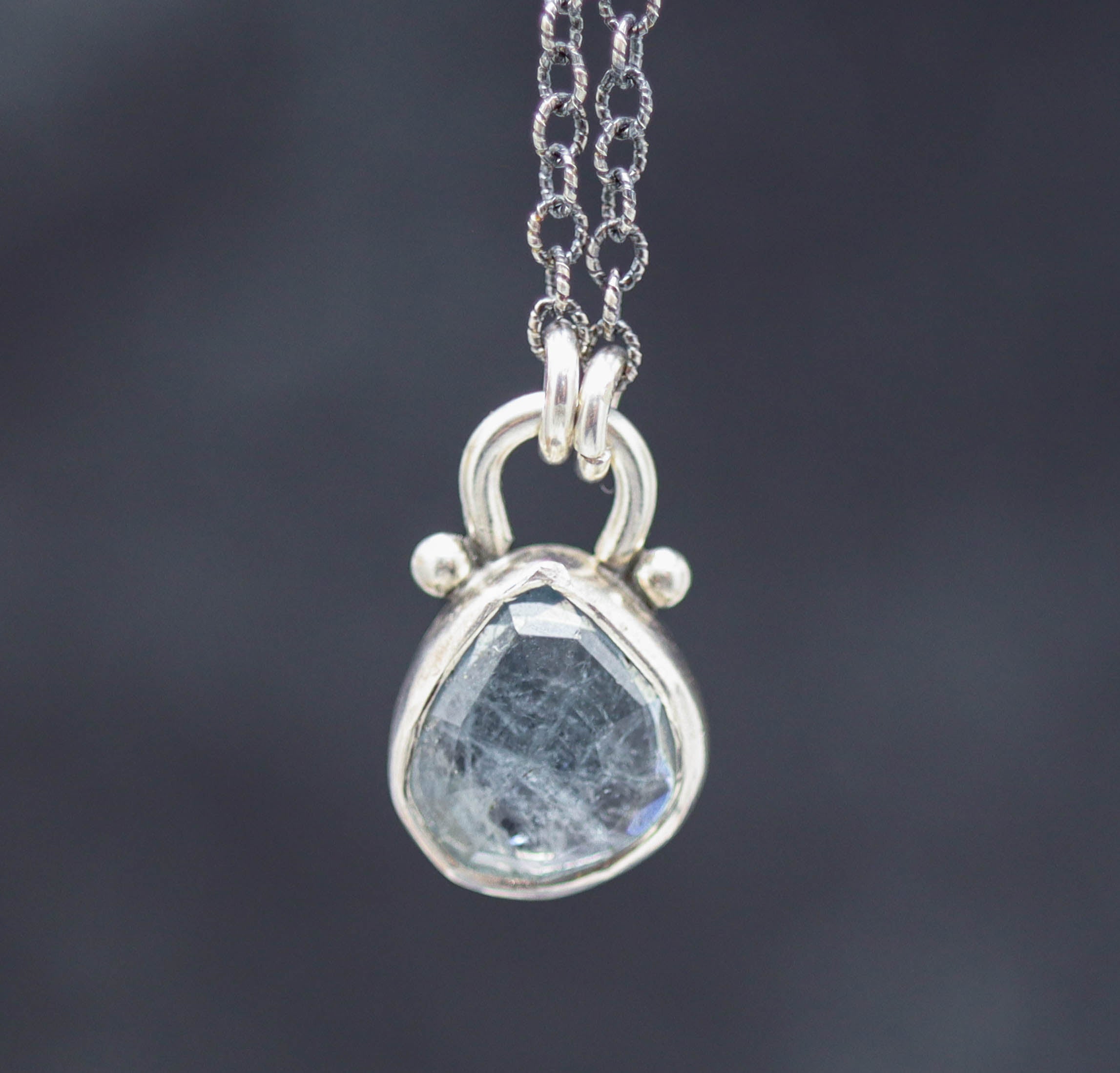A sterling silver pendant necklace featuring a rose-cut blue tourmaline gemstone, attached to an oxidized cable link chain.