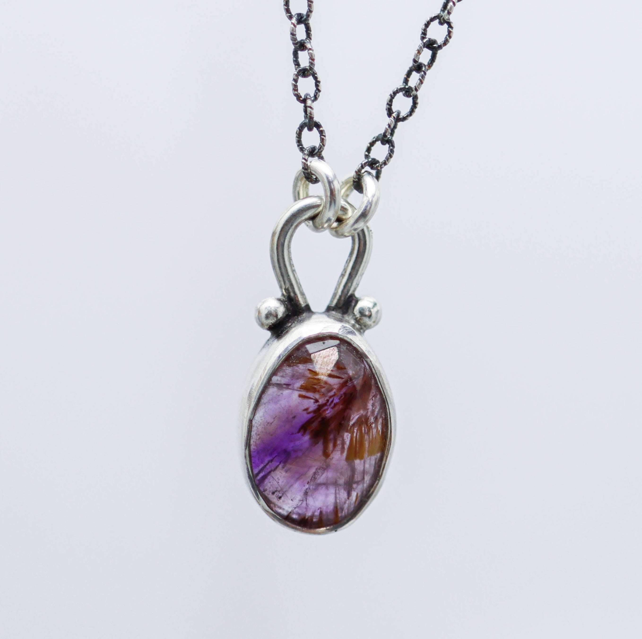 A sterling silver pendant necklace featuring a faceted rose cut super seven gemstone with small silver ball accents, displayed on a silver oxidized cable link chain with a lobster claw closure.