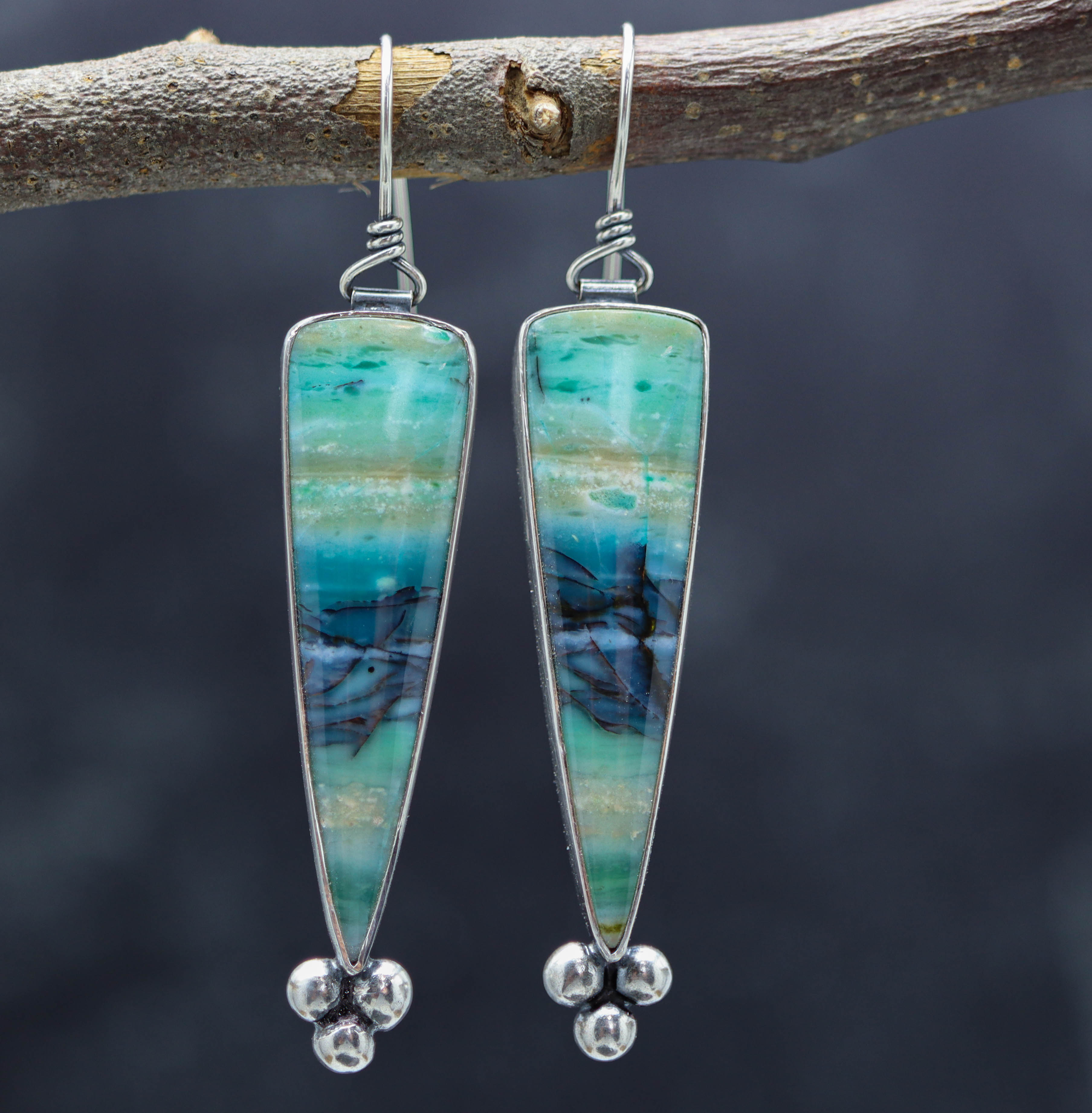A pair of sterling silver dangle earrings with opalized petrified wood stones, displayed against a dark background.