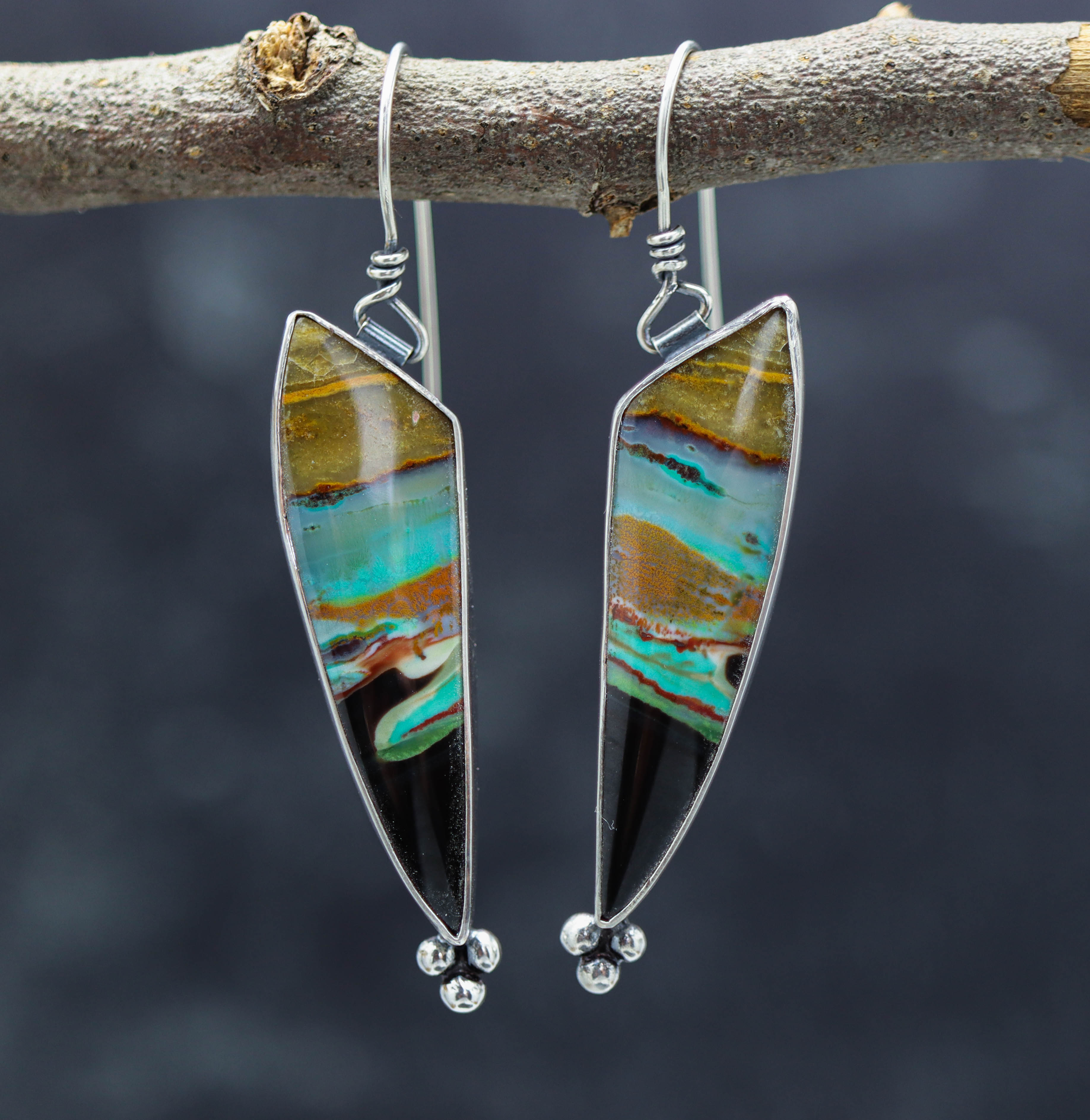 A pair of sterling silver dangle earrings featuring an opalized petrified wood design, with a black and multicolored stone.