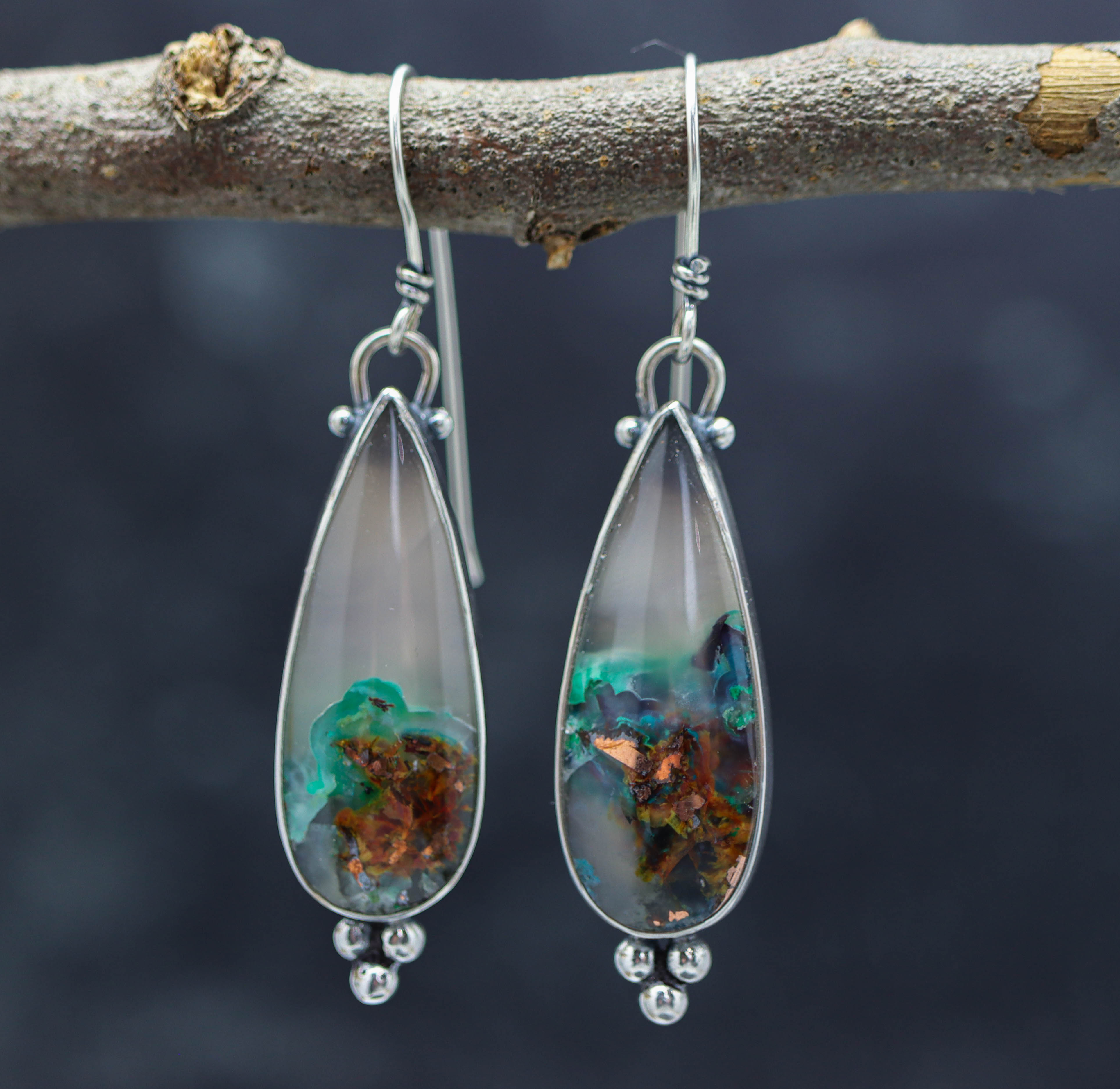 A pair of sterling silver dangle earrings with confetti chrysocolla stones, displayed against a natural outdoor background.