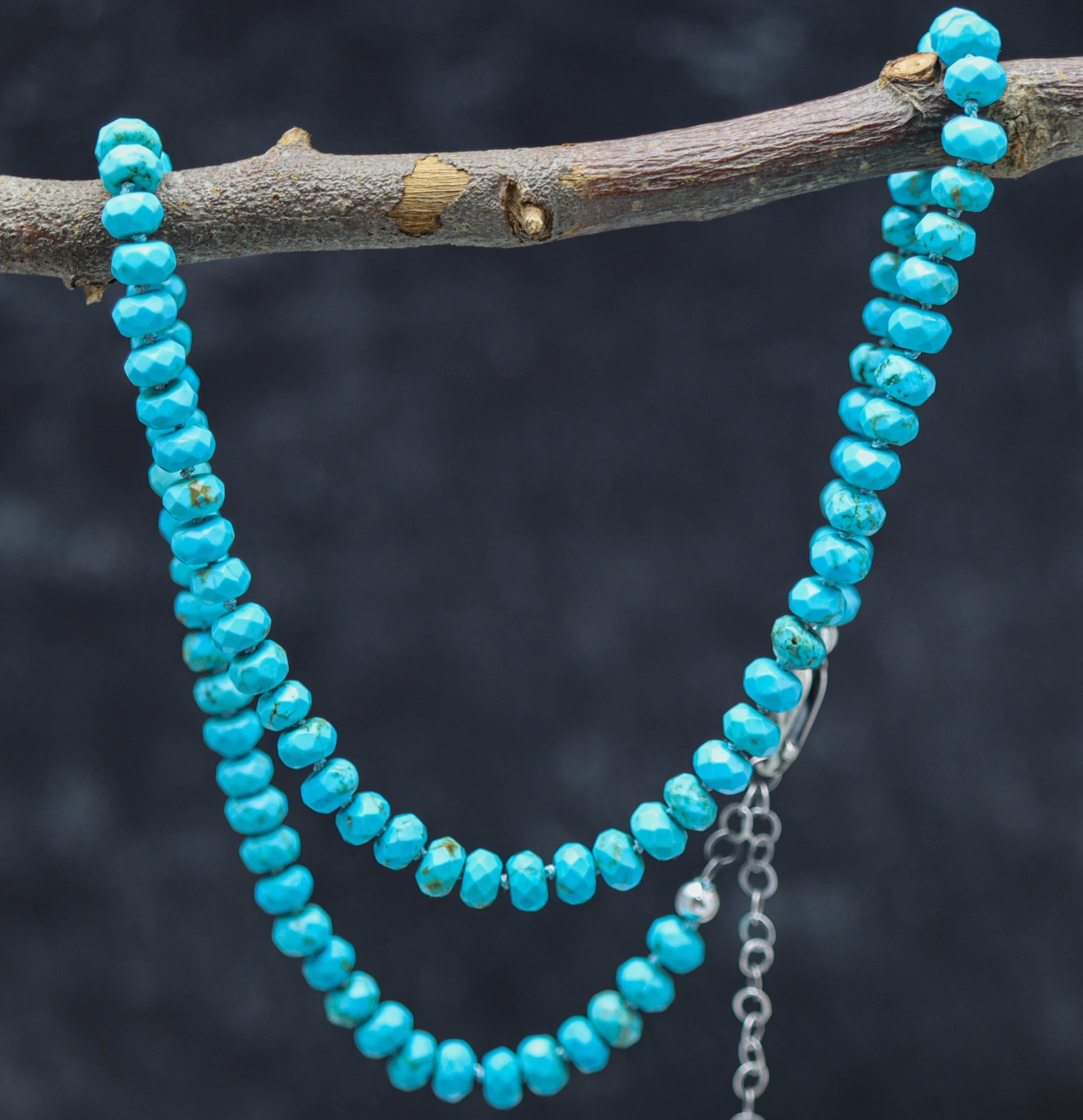 A sterling silver necklace with a strand of faceted turquoise hand-knotted beads, displayed against a dark background with a blurred branch in the background.