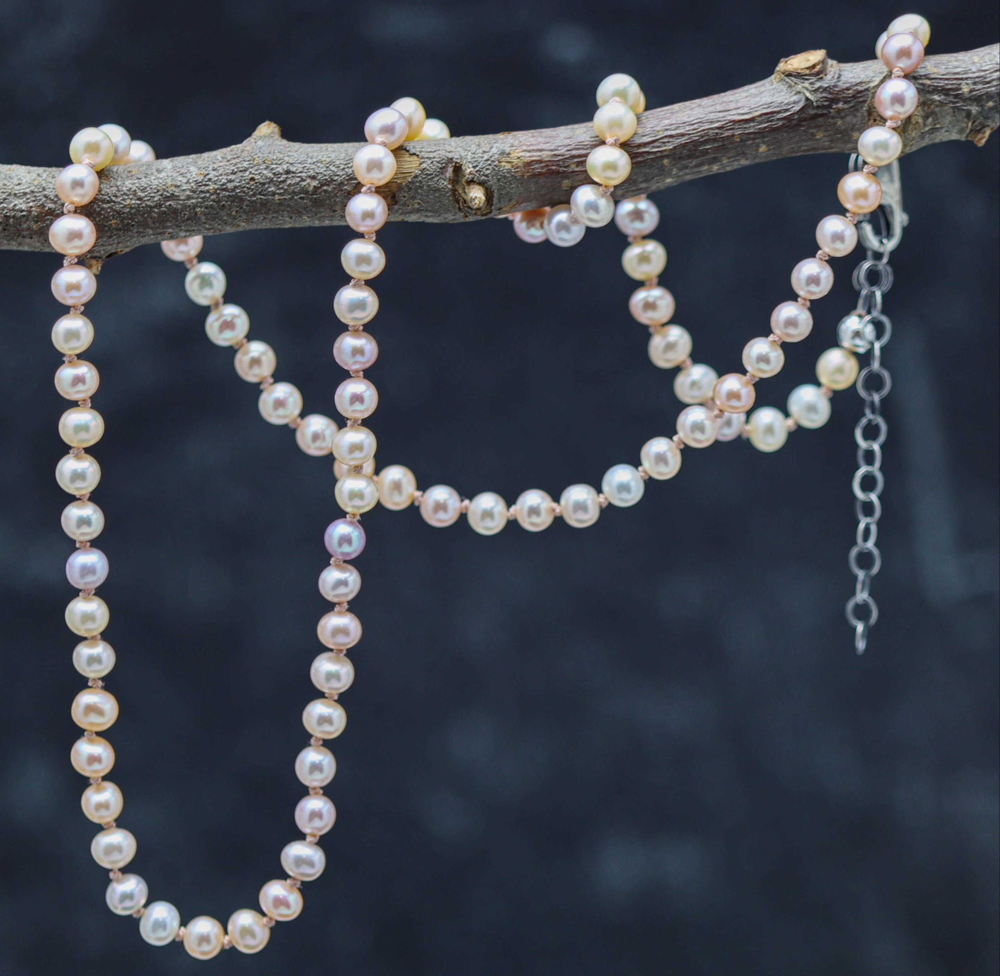 A sterling silver necklace featuring hand knotted strands of pink pearl beads, with a lobster claw closure, displayed against a dark background.