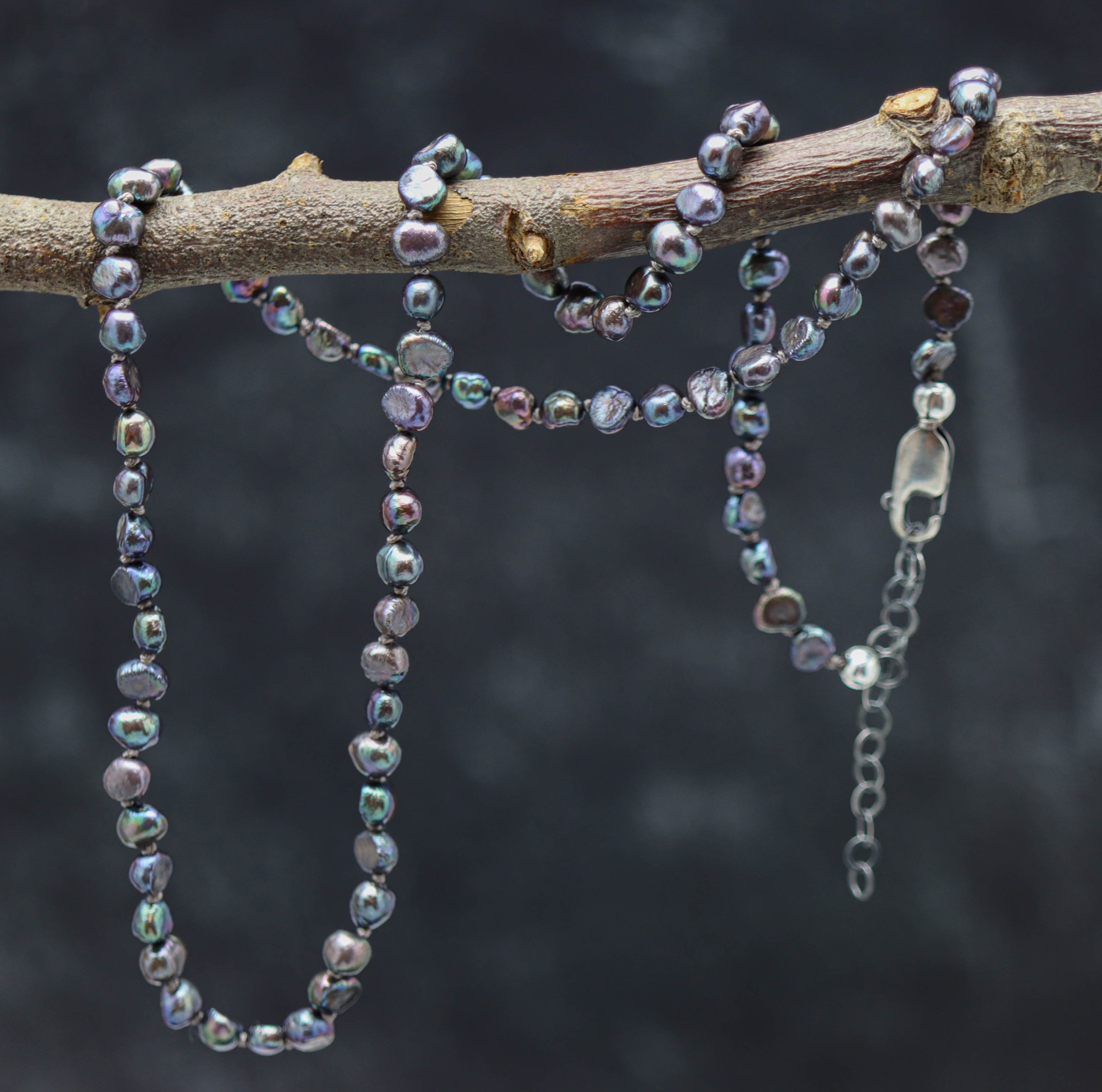 A sterling silver necklace featuring hand knotted strands of peacock freshwater pearl beads with a lobster claw closure.