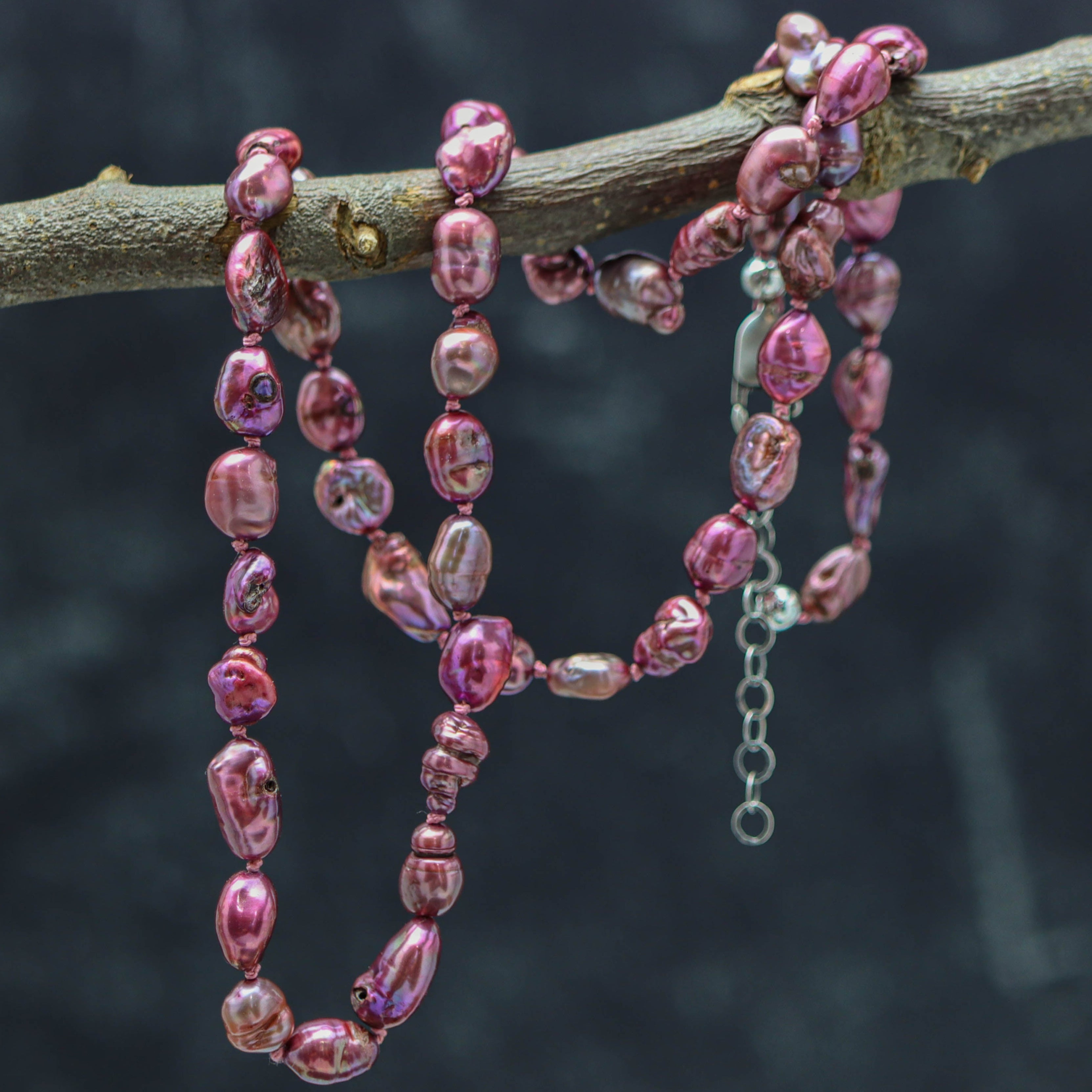 Pink beaded necklace draped over a branch with a blurred dark background