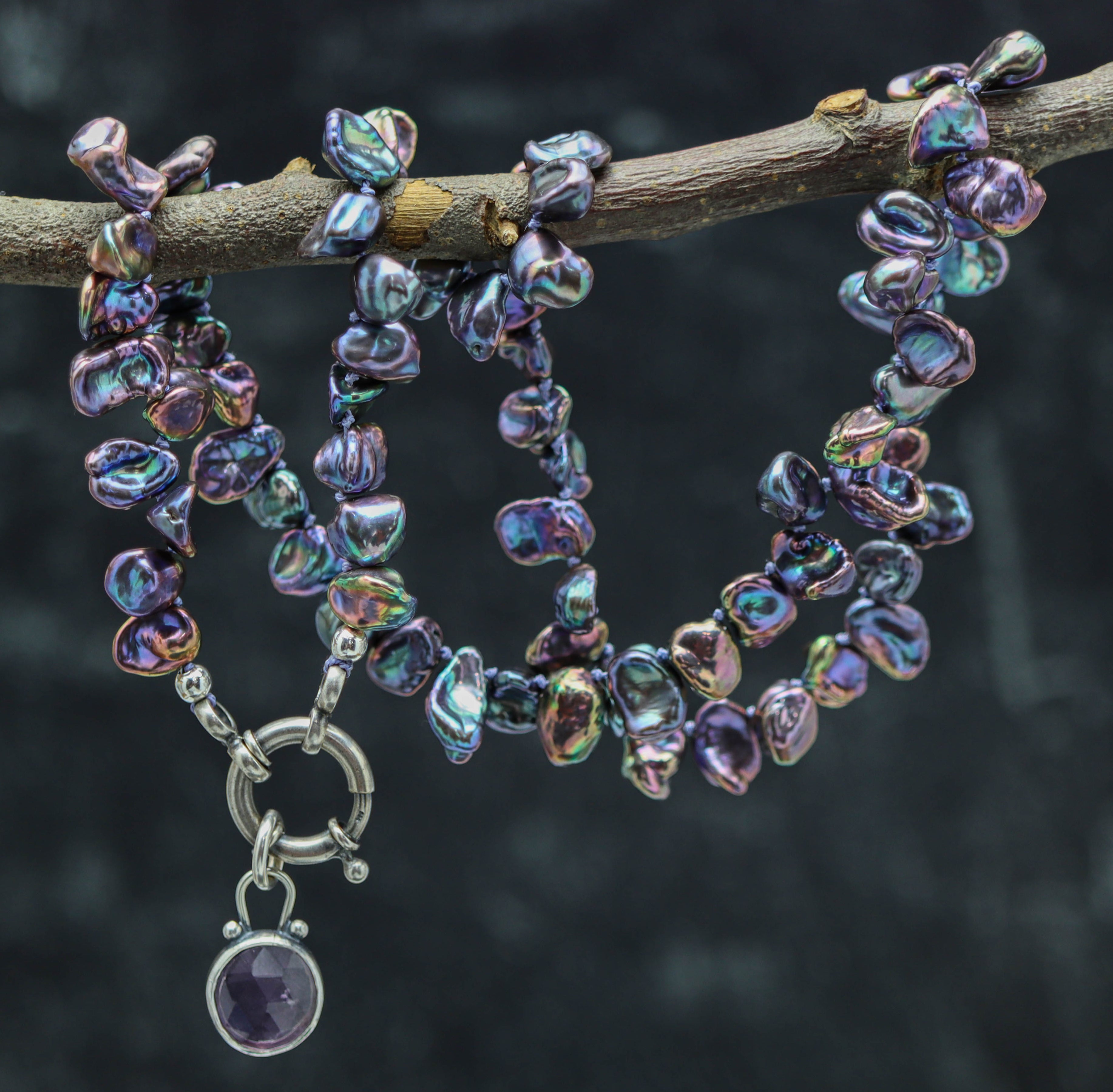 Peacock Pearl necklace with a silver clasp on a branch against a dark background