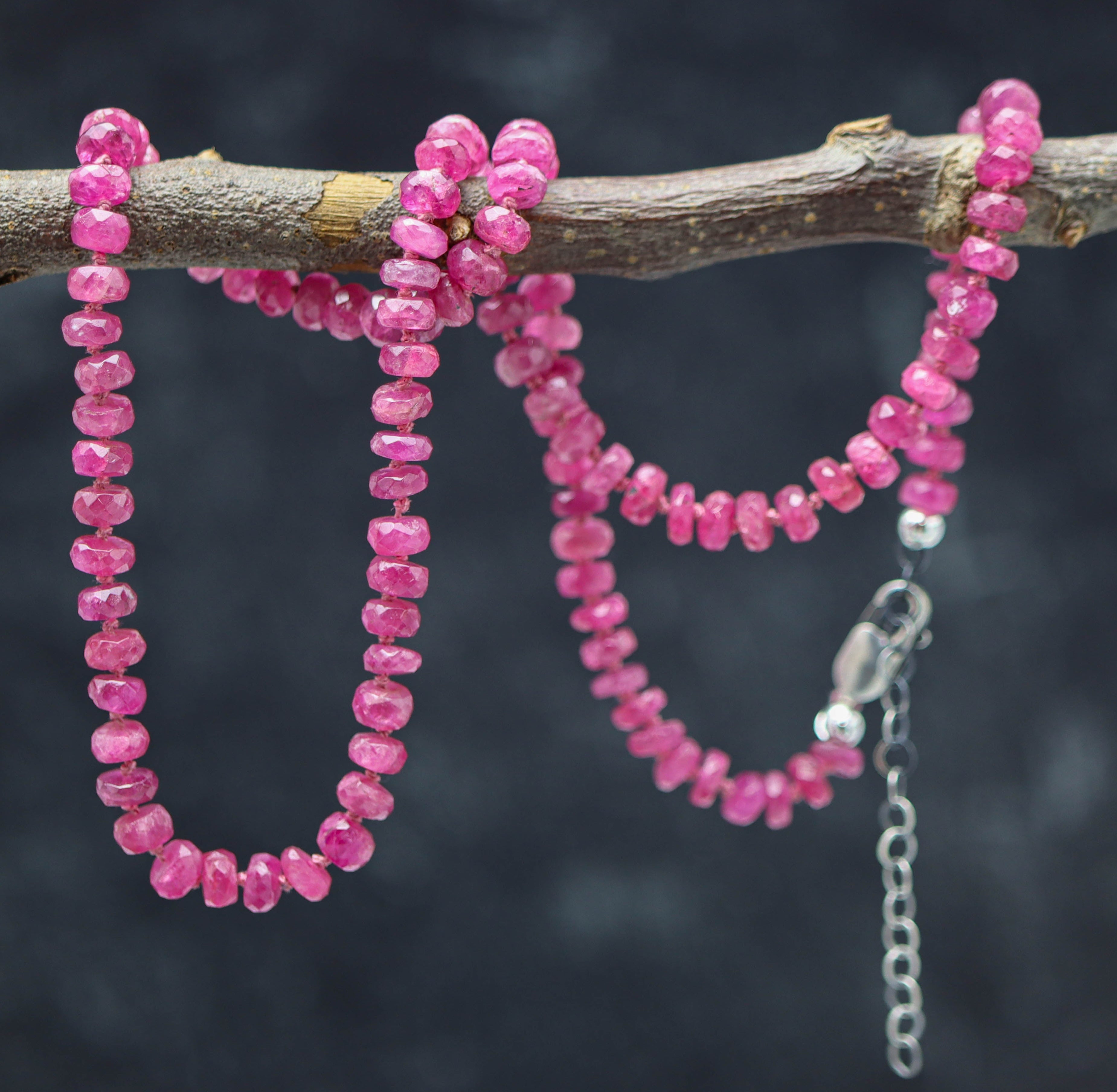 A hand knotted pink tourmaline bead necklace with sterling silver closure on a dark background.