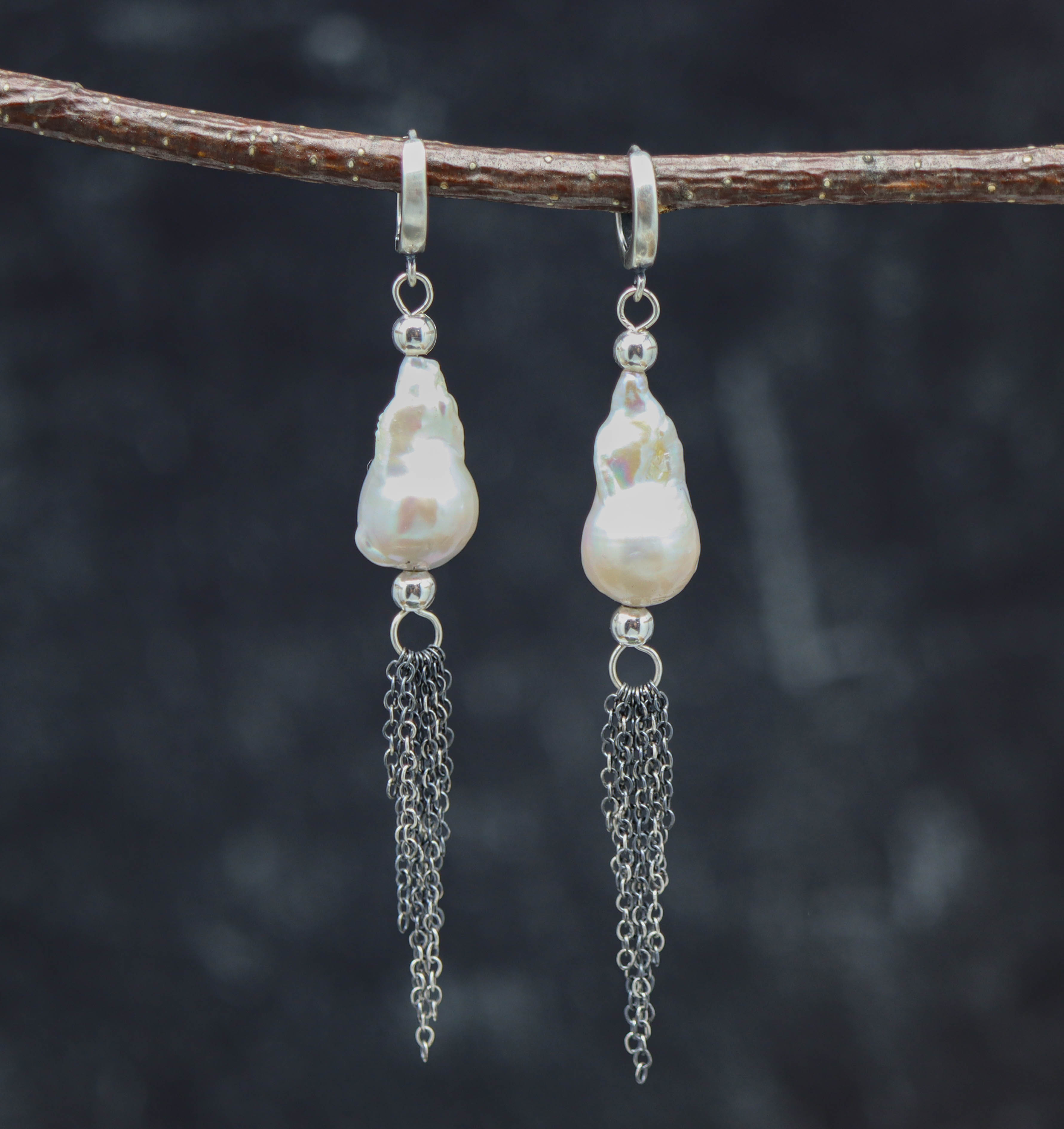 A pair of sterling silver baroque pearl dangle fringe earrings displayed on a branch against a dark background.
