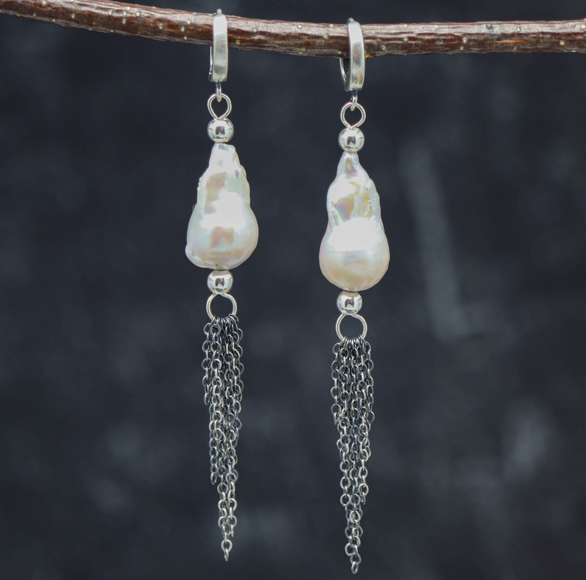 A pair of sterling silver baroque pearl dangle fringe earrings displayed on a branch against a dark background.