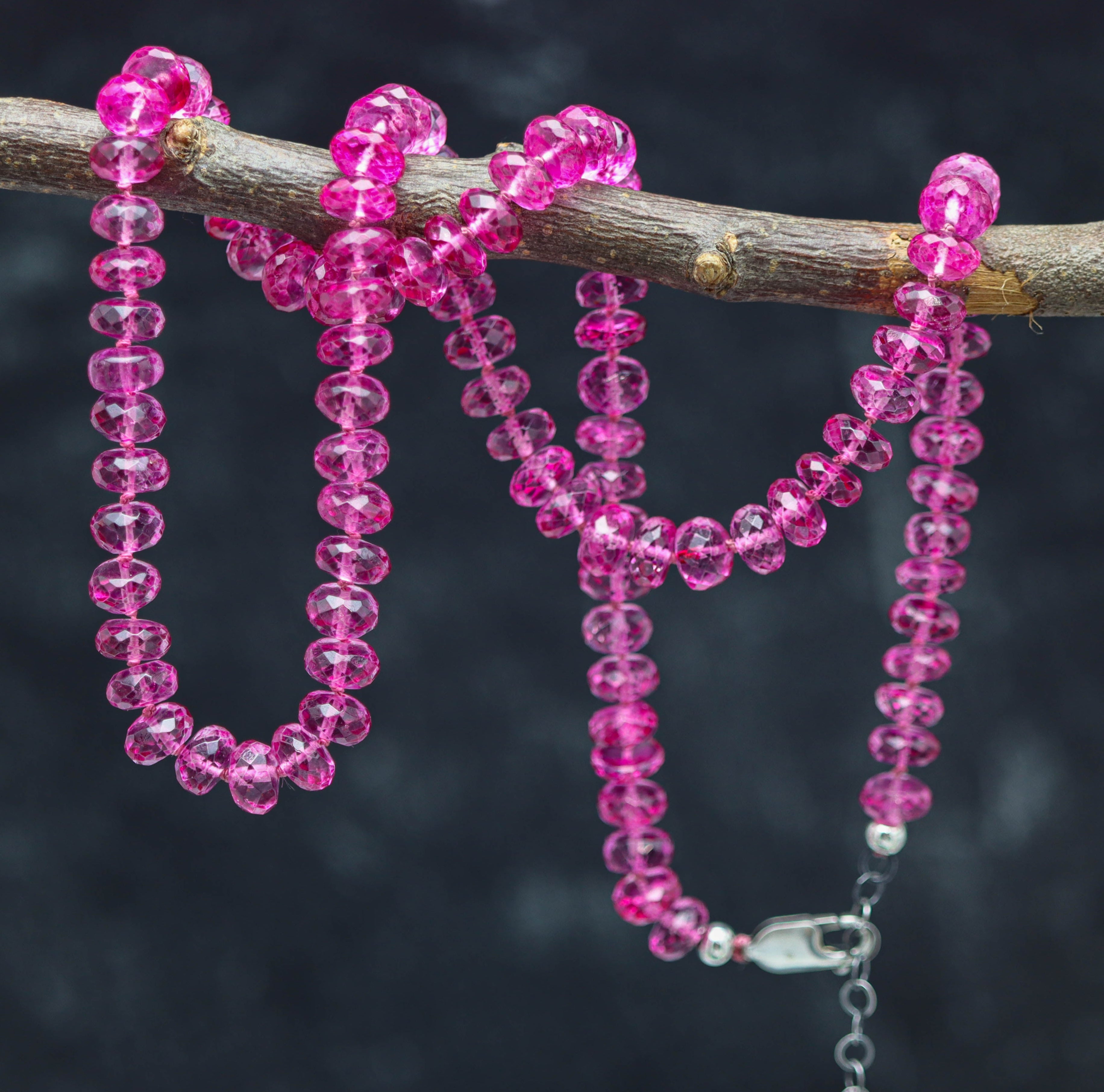 A hand knotted necklace with pink beads, displayed on a branch, with a sterling silver clasp.