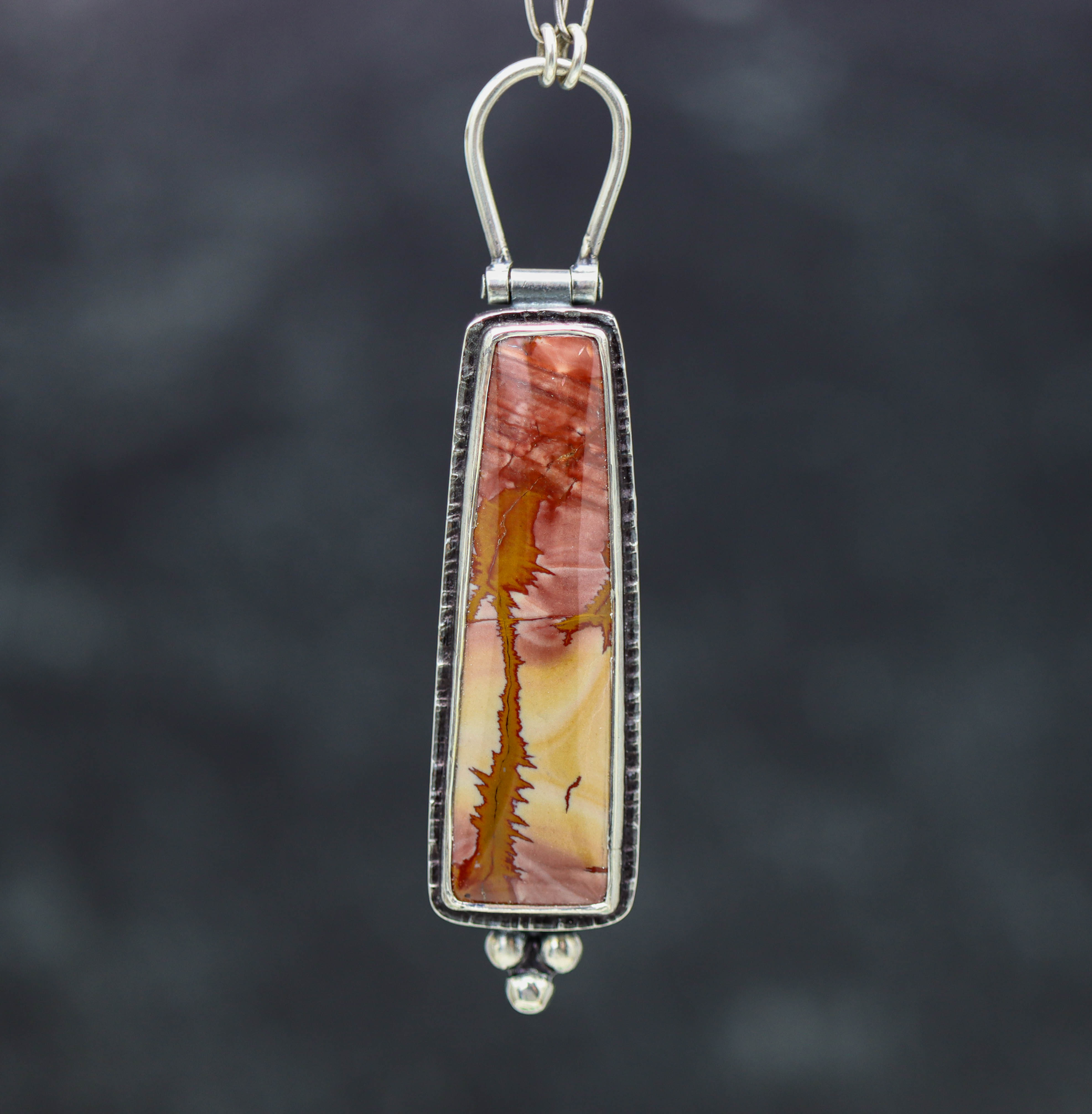 A red falcon jasper pendant with a sterling silver setting, attached to an oval link chain.