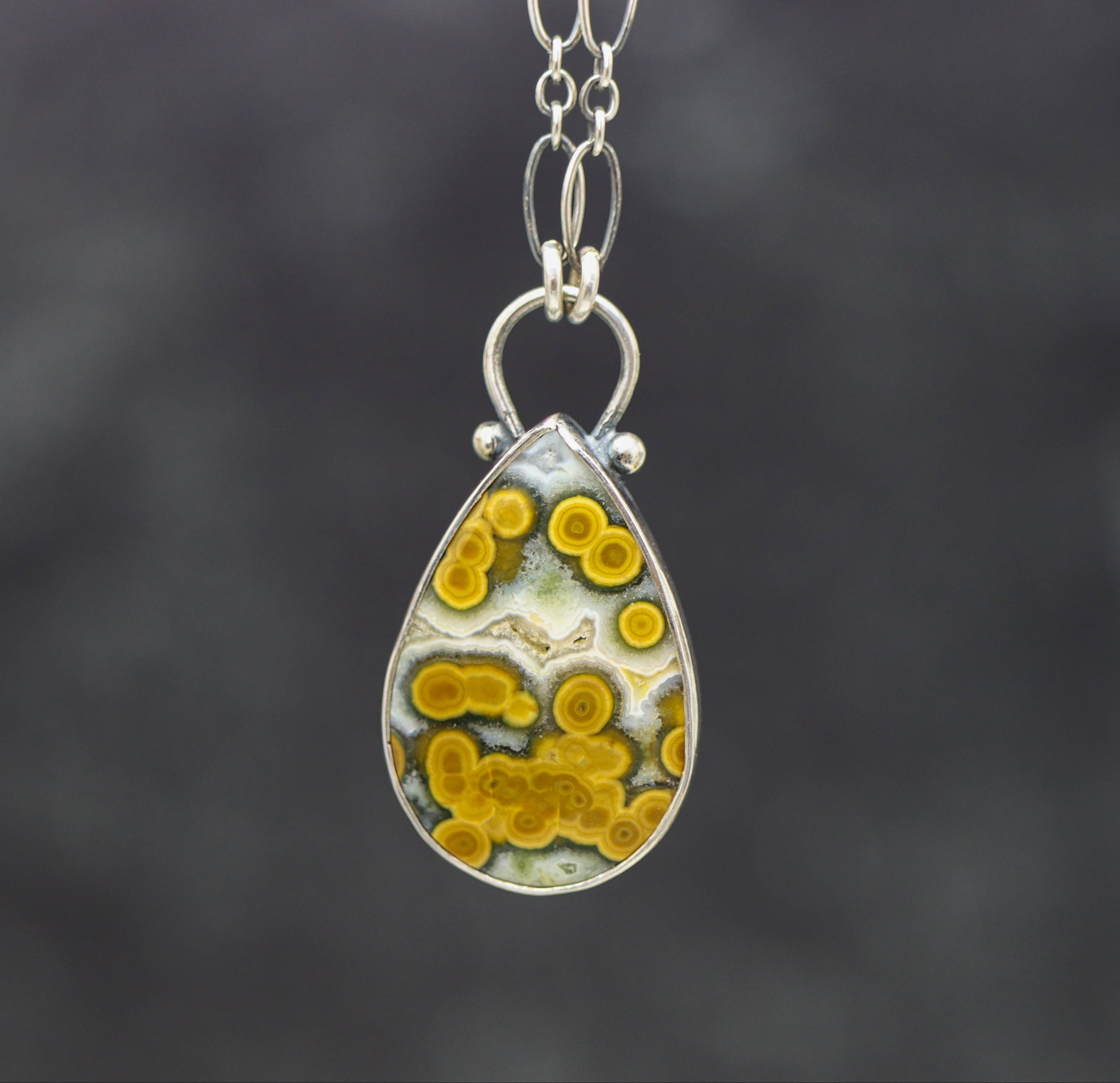 Teardrop-shaped pendant with yellow and white pattern on a dark background
