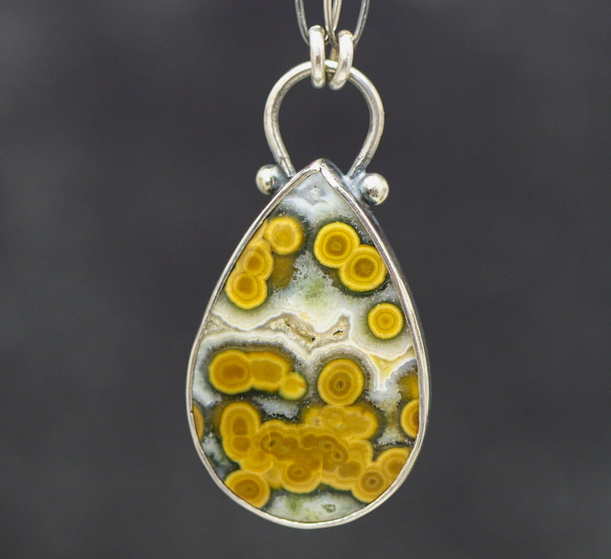 Teardrop-shaped pendant with yellow and white pattern on a dark background