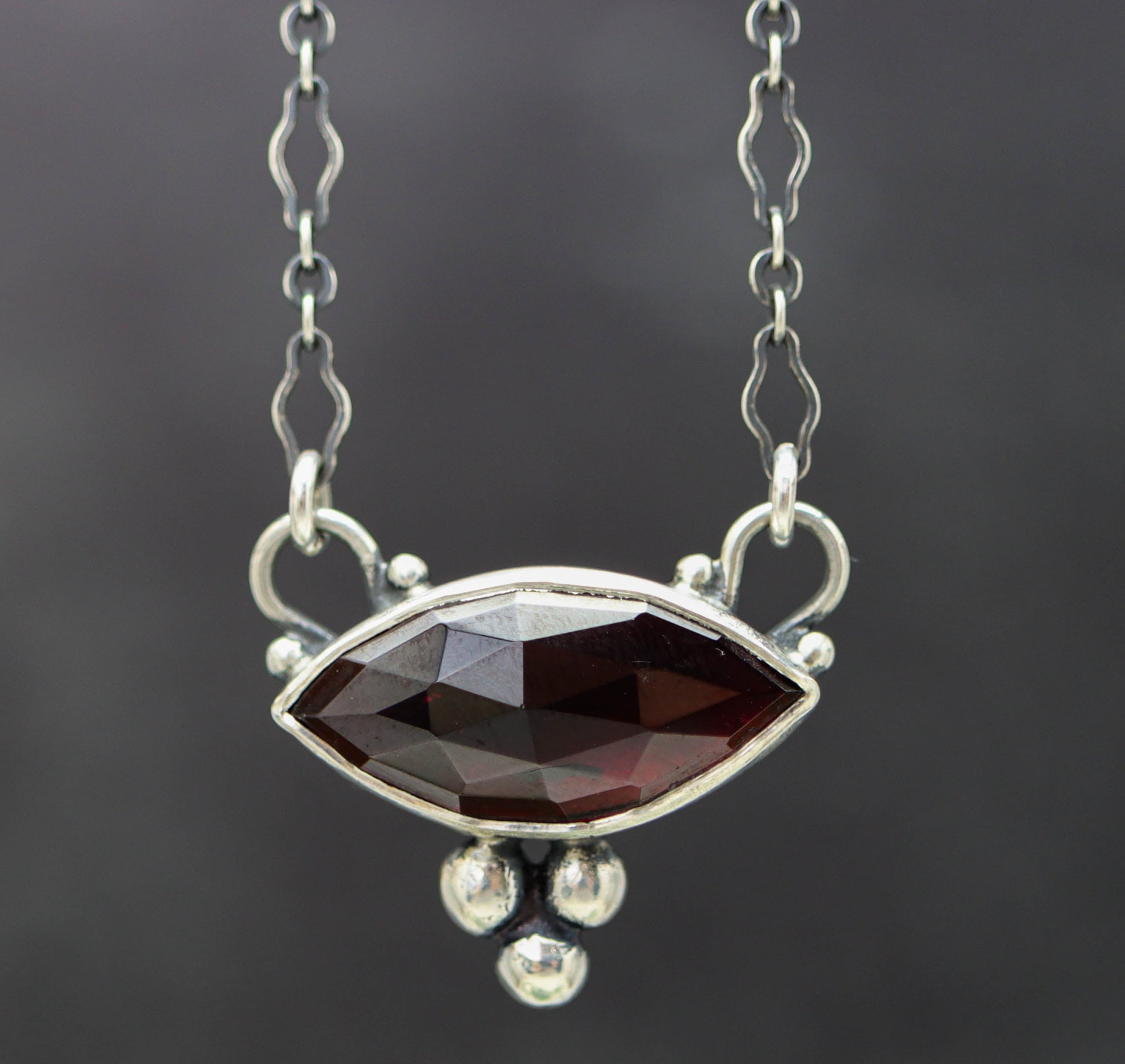 A sterling silver pendant necklace with a garnet centerpiece and small silver ball accents, displayed on a chain.