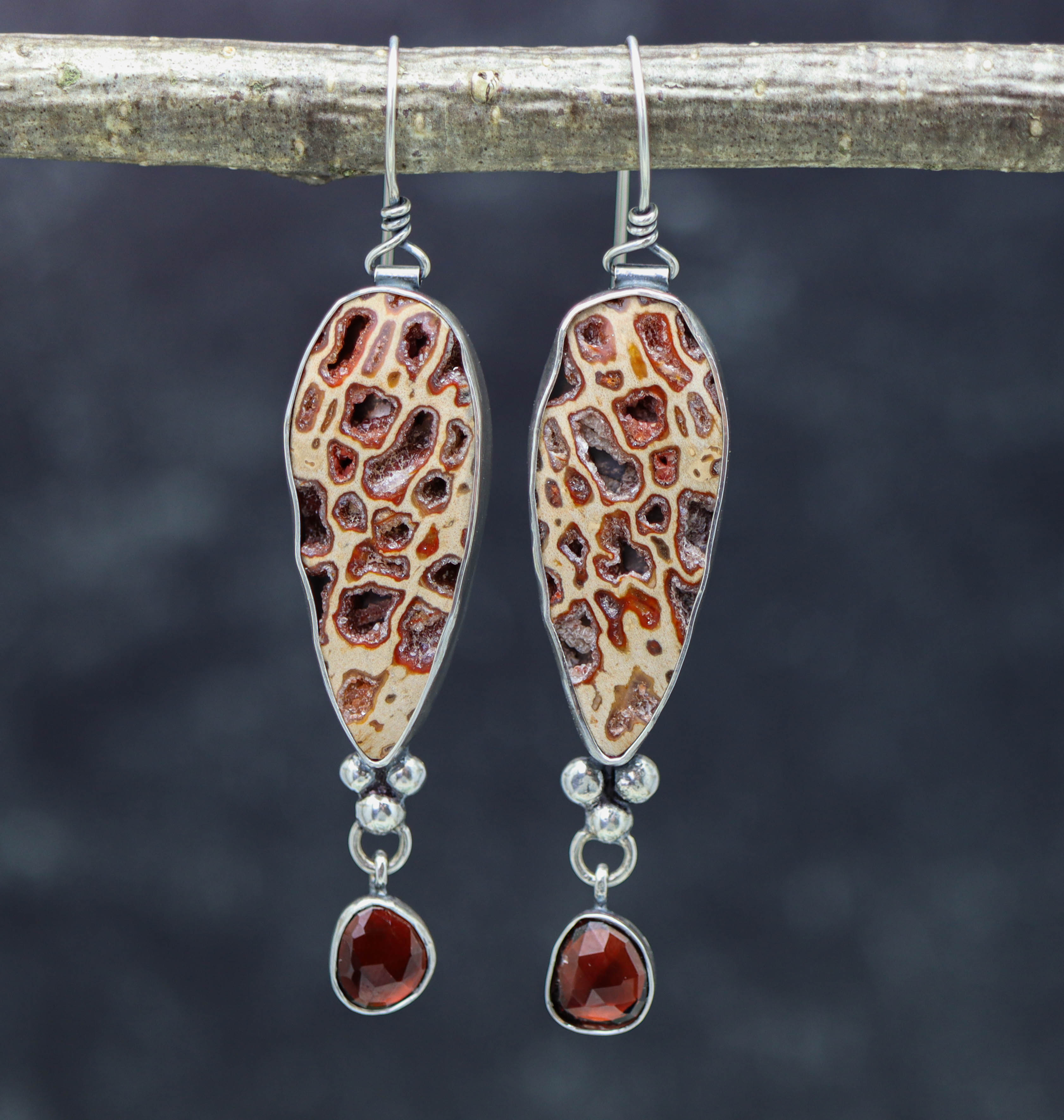 A pair of sterling silver dangle earrings featuring petrified wood and garnet stones with crystal embellishments.