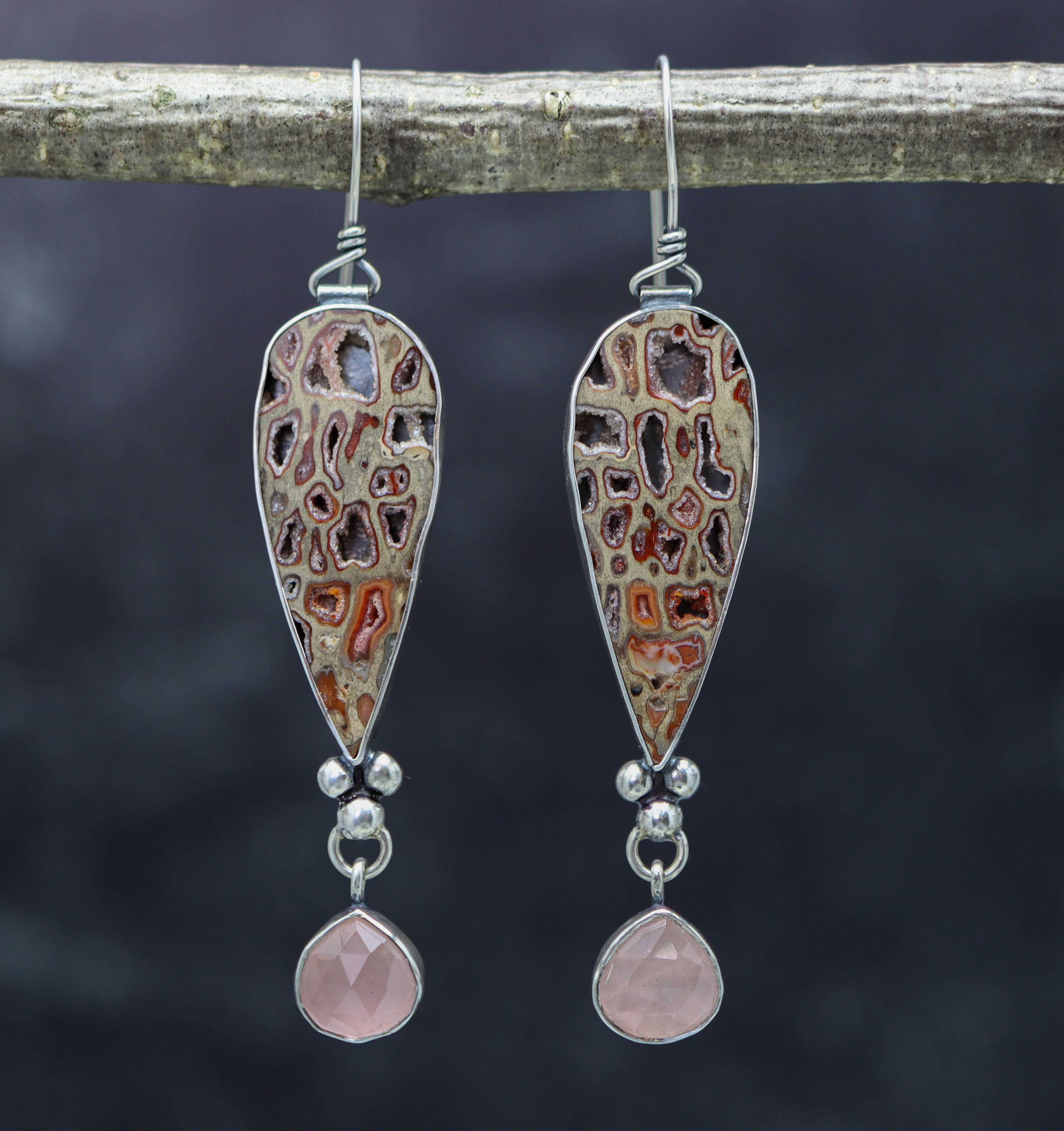 A pair of sterling silver dangle earrings with petrified wood and rose quartz, displayed against a dark background.