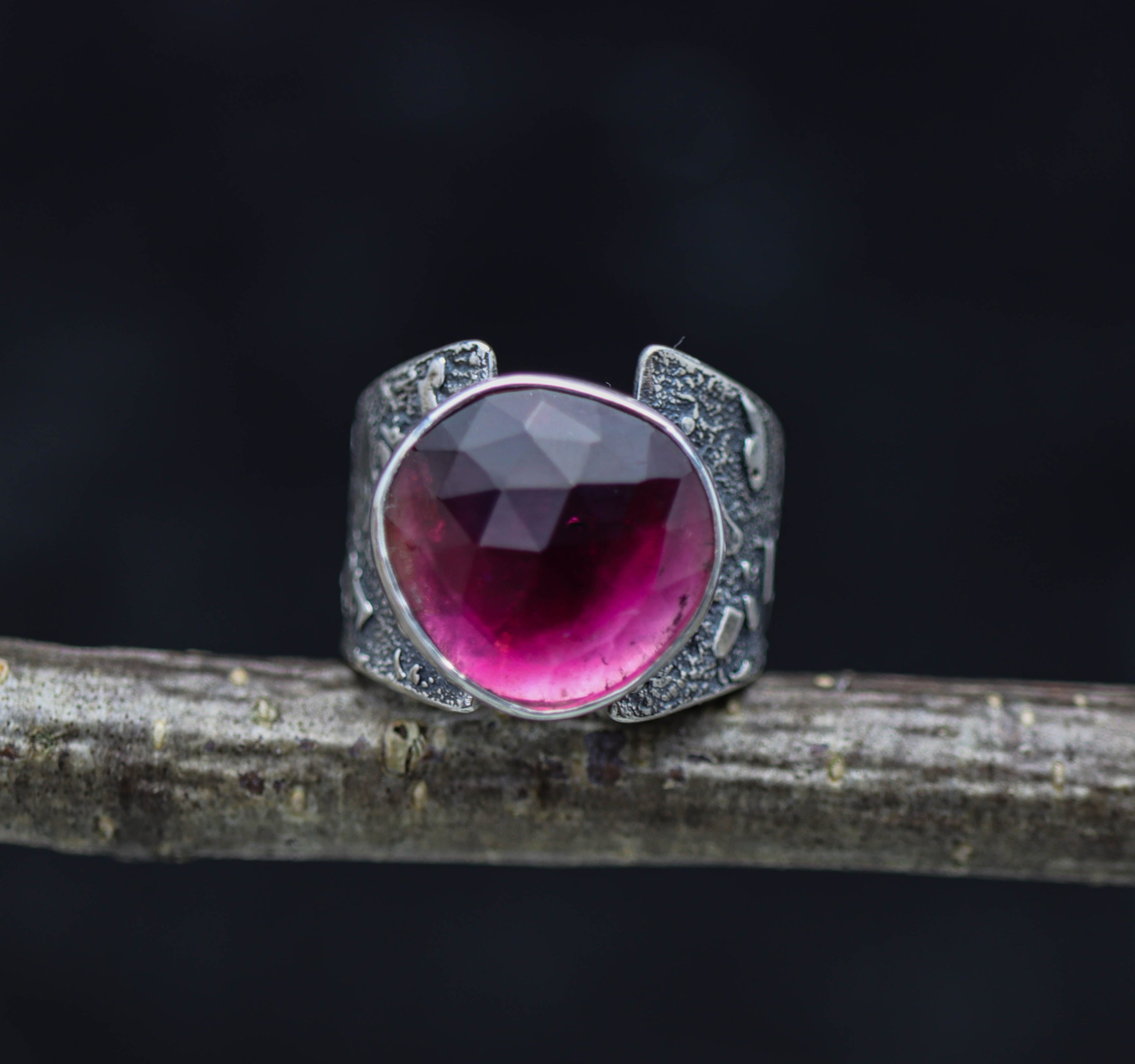 A wide band sterling silver ring with a large pink tourmaline rose cut in the center, featuring texture and patina details on the band.