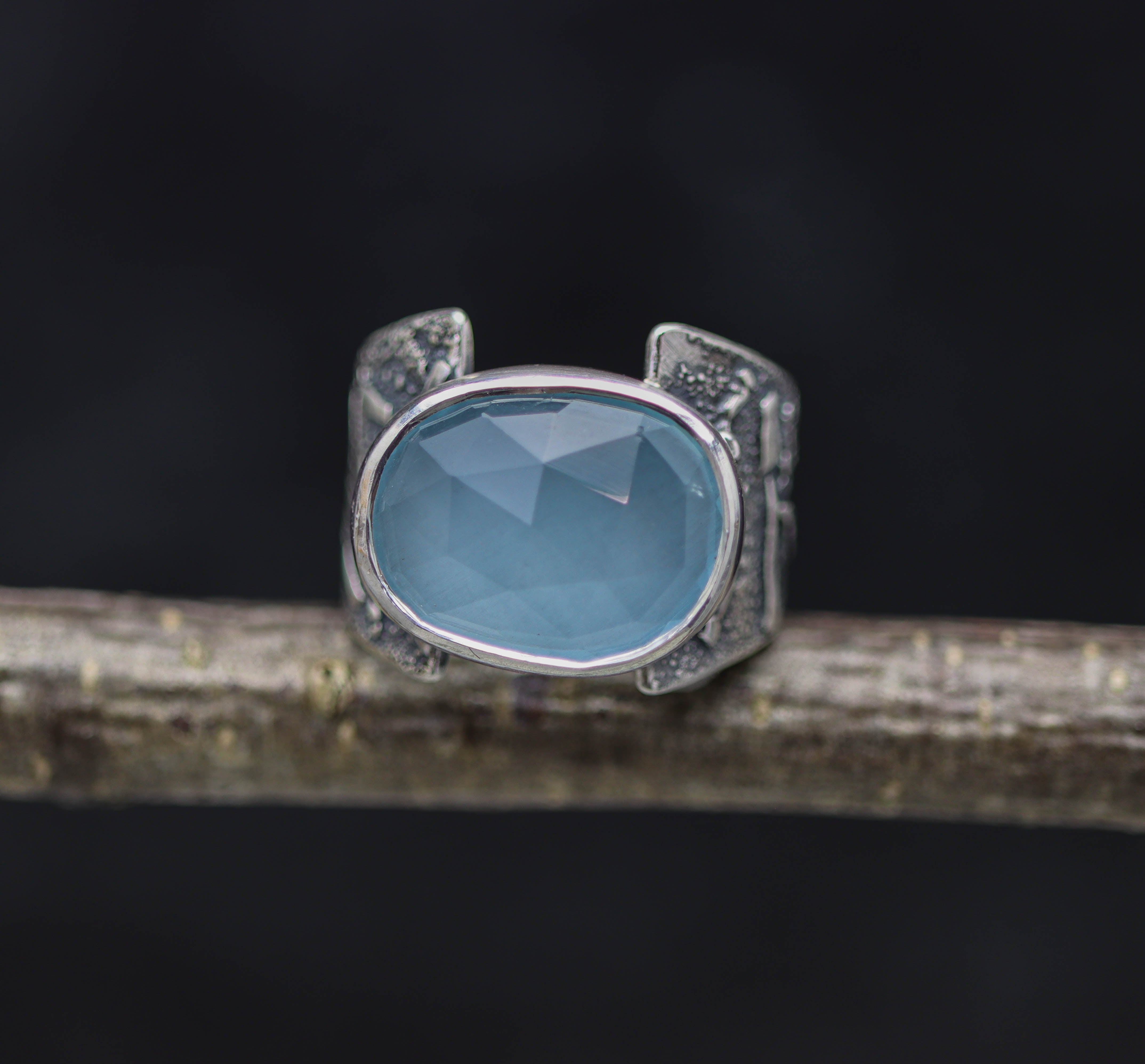 A sterling silver wide band ring with a rose cut aqua chalcedony stone set on a dark background, appearing blue-green in color.