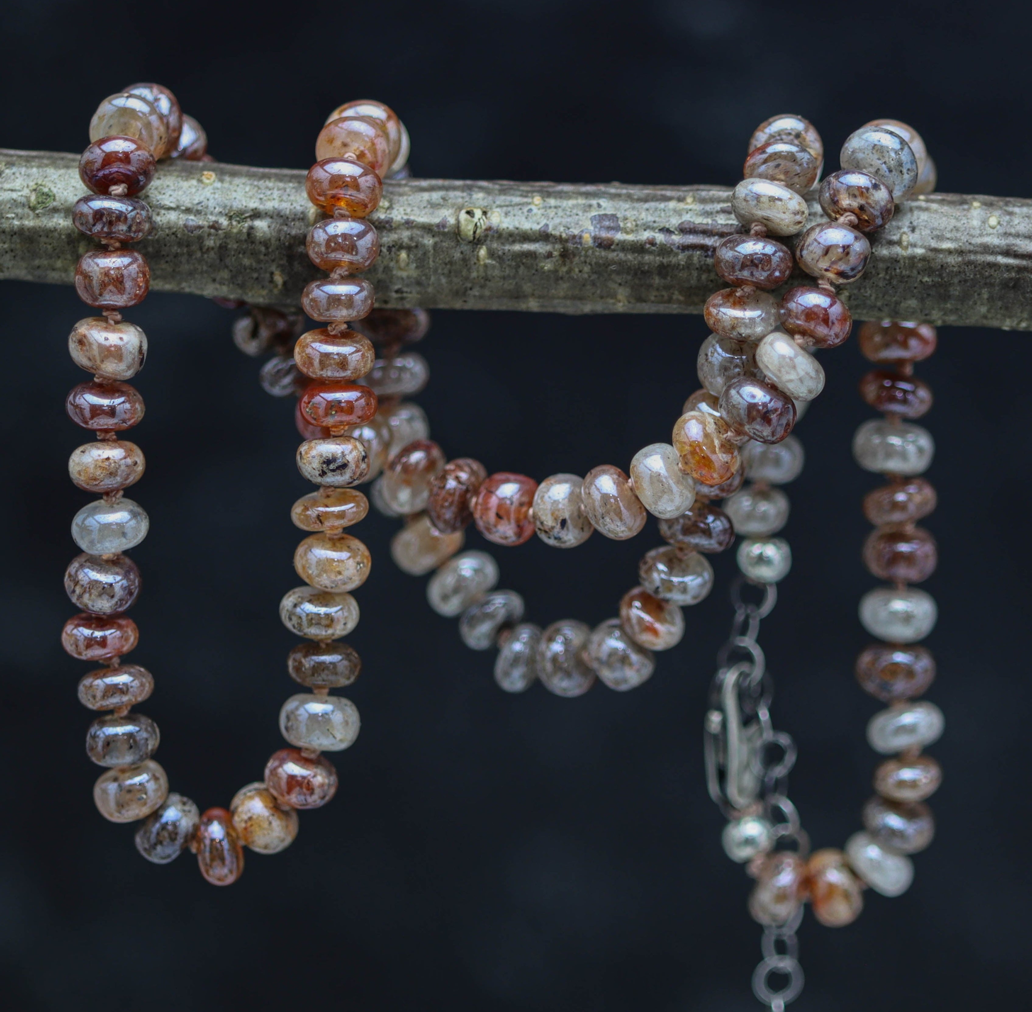 A hand knotted bead necklace with sterling silver and moonstone beads, displayed on a branch against a dark background.