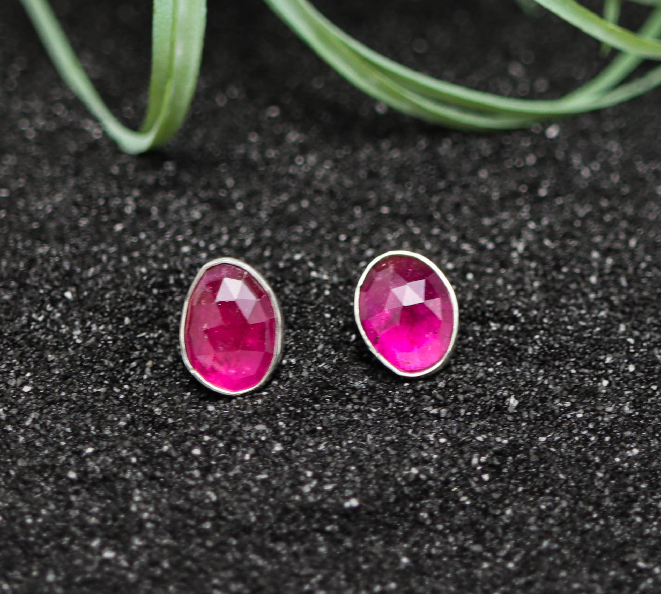 Pink stud earrings on a black surface with greenery in the background