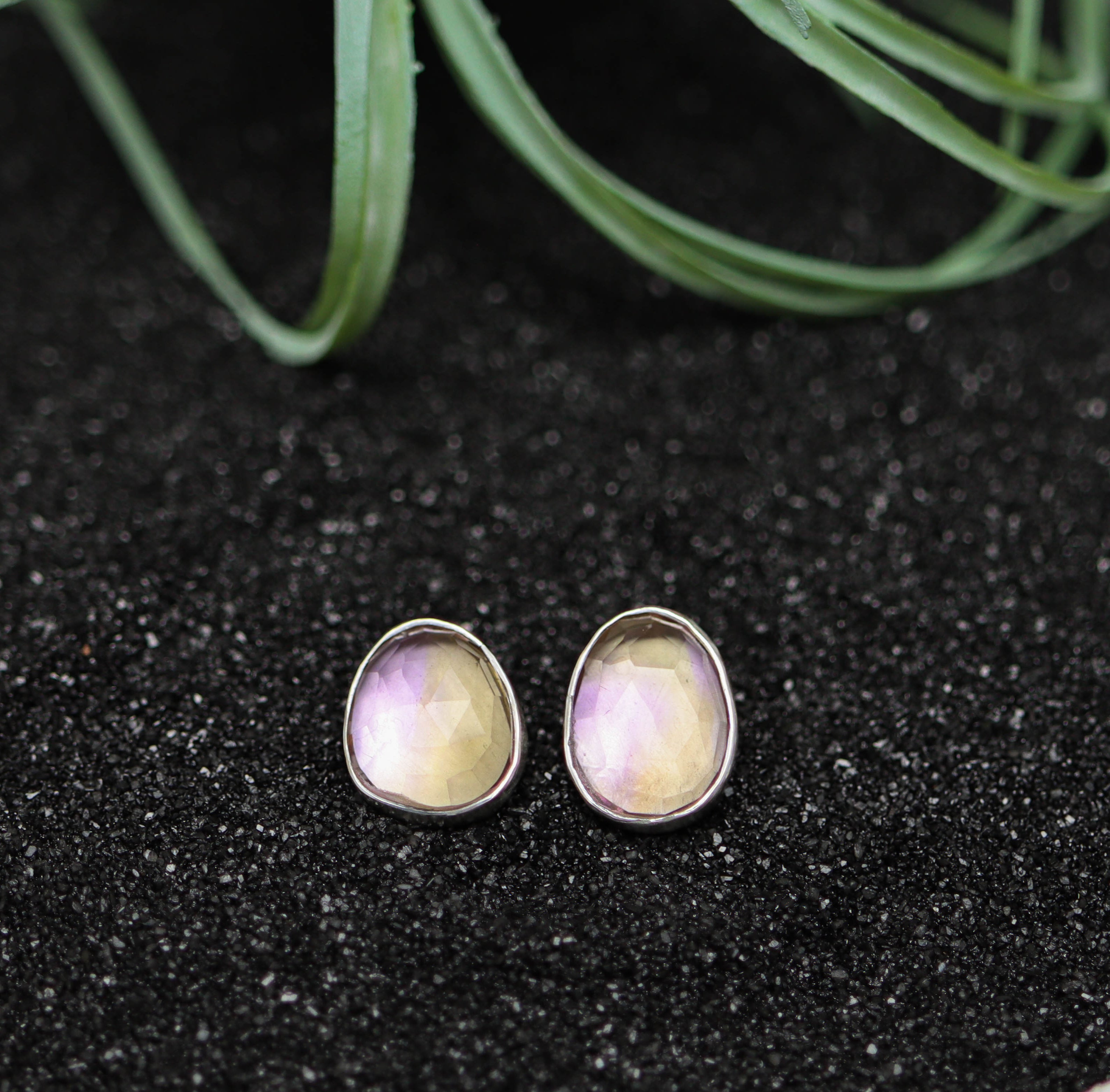 Pair of earrings with a purple and yellow gemstone on a black surface.