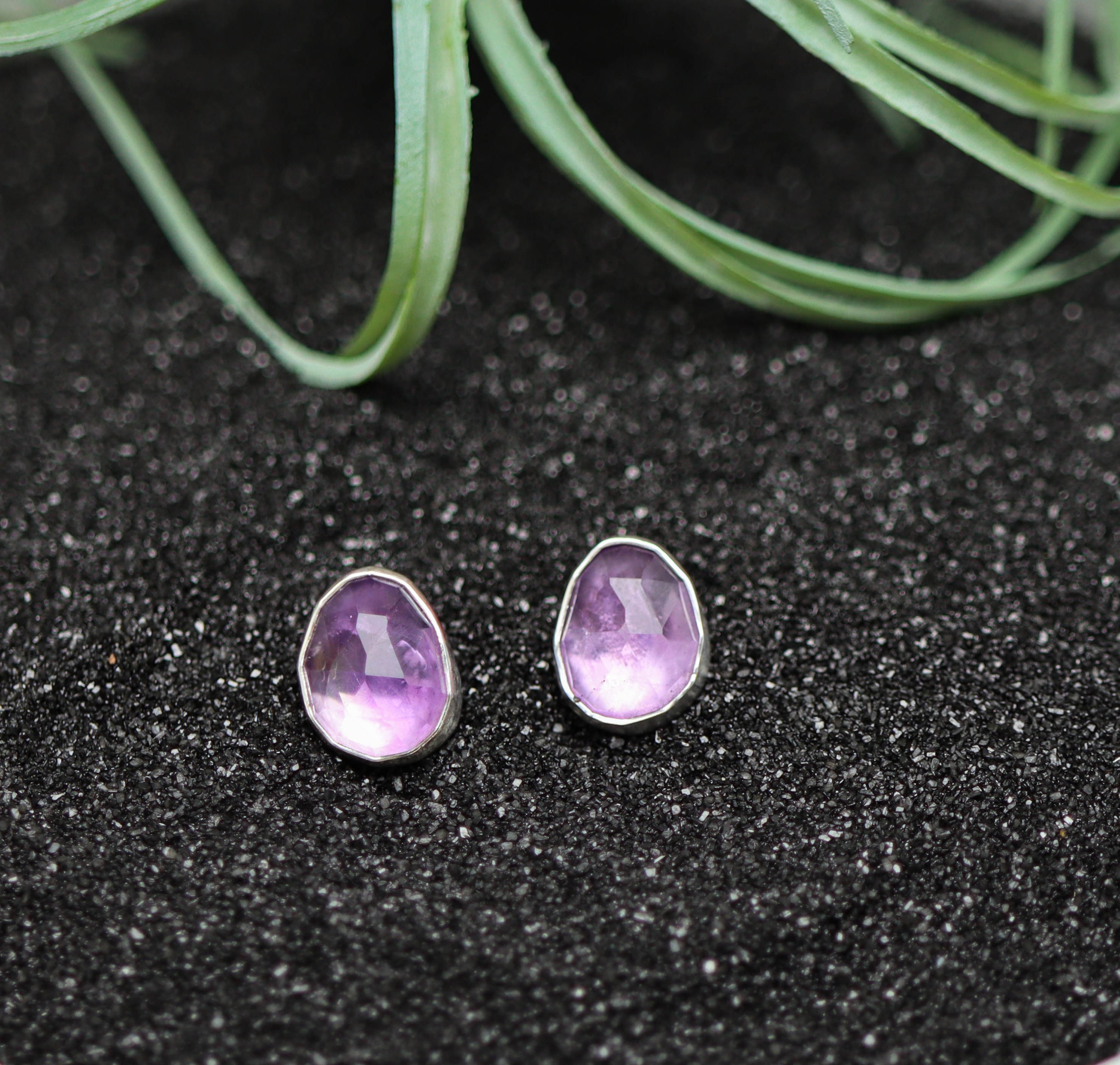Purple teardrop earrings on a black glittery surface with greenery in the background