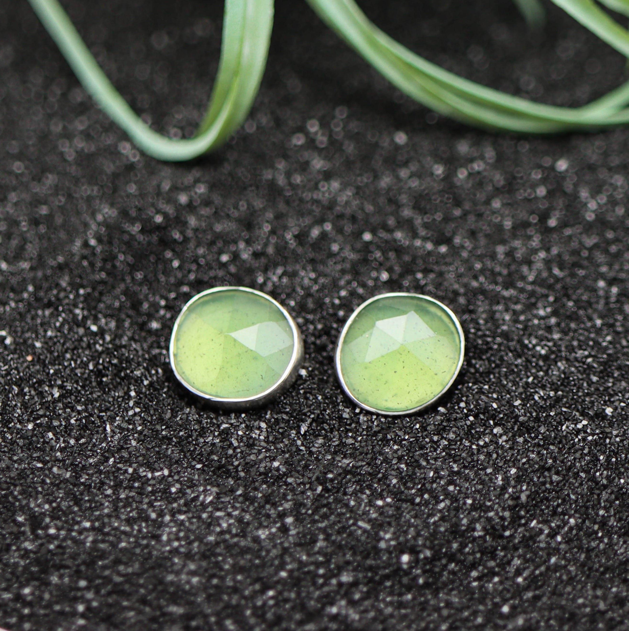Green round earrings on a black textured surface with green leaves in the background