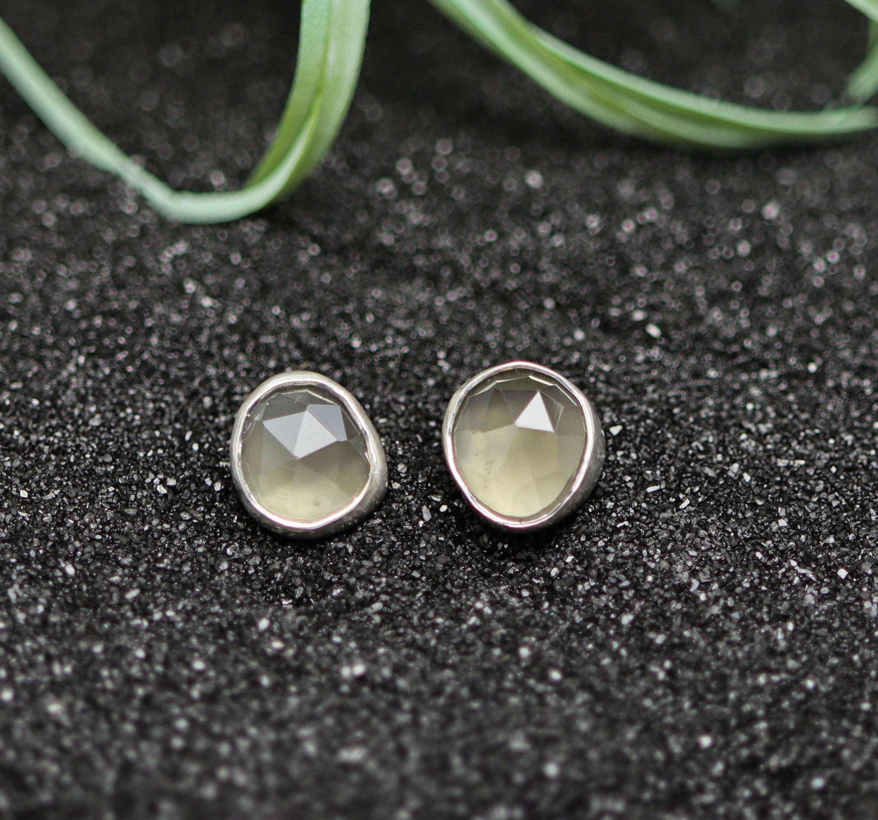 Pair of silver earrings with grey gemstones on a black textured surface.