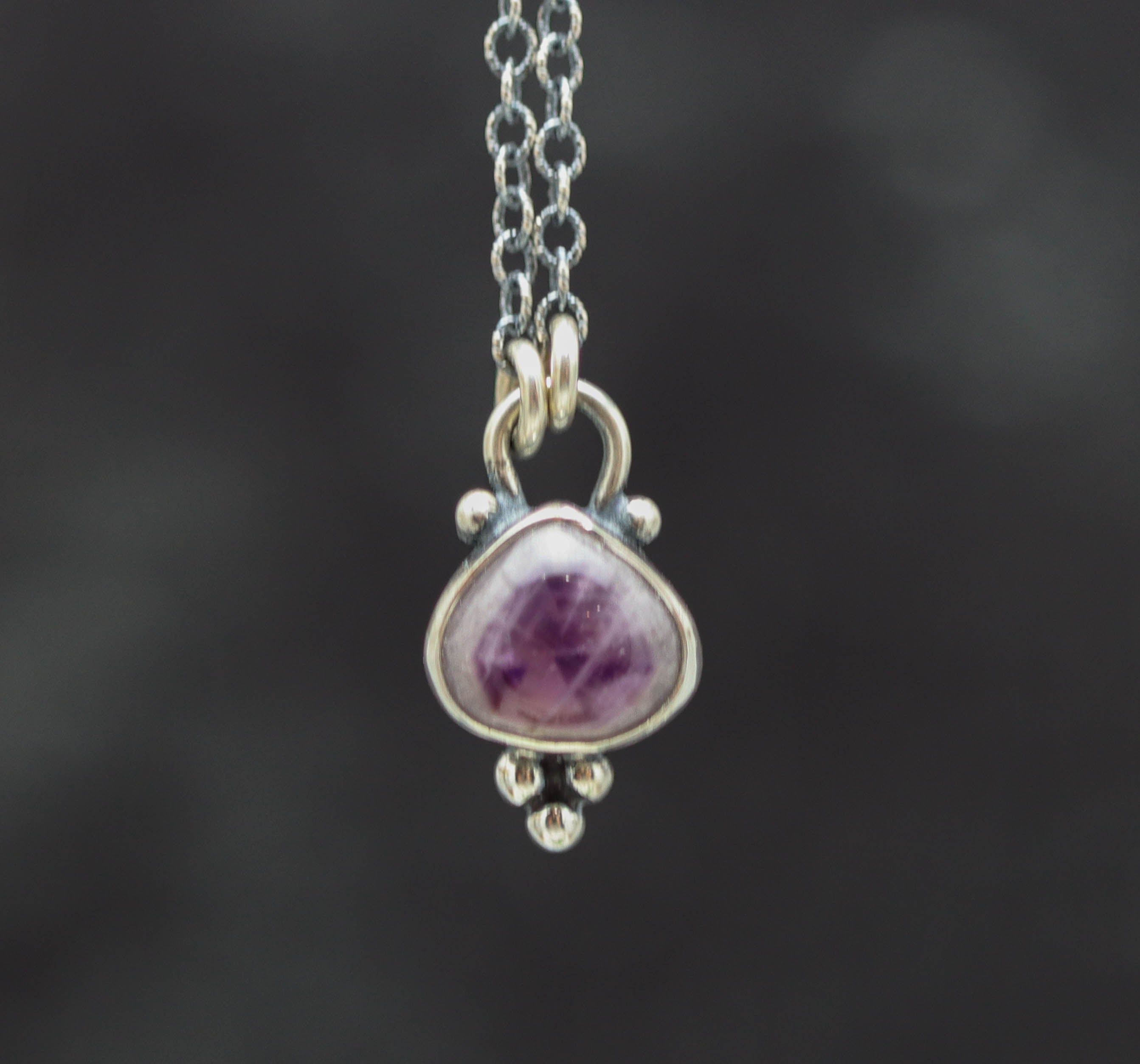 Silver pendant with a purple gemstone on a dark background